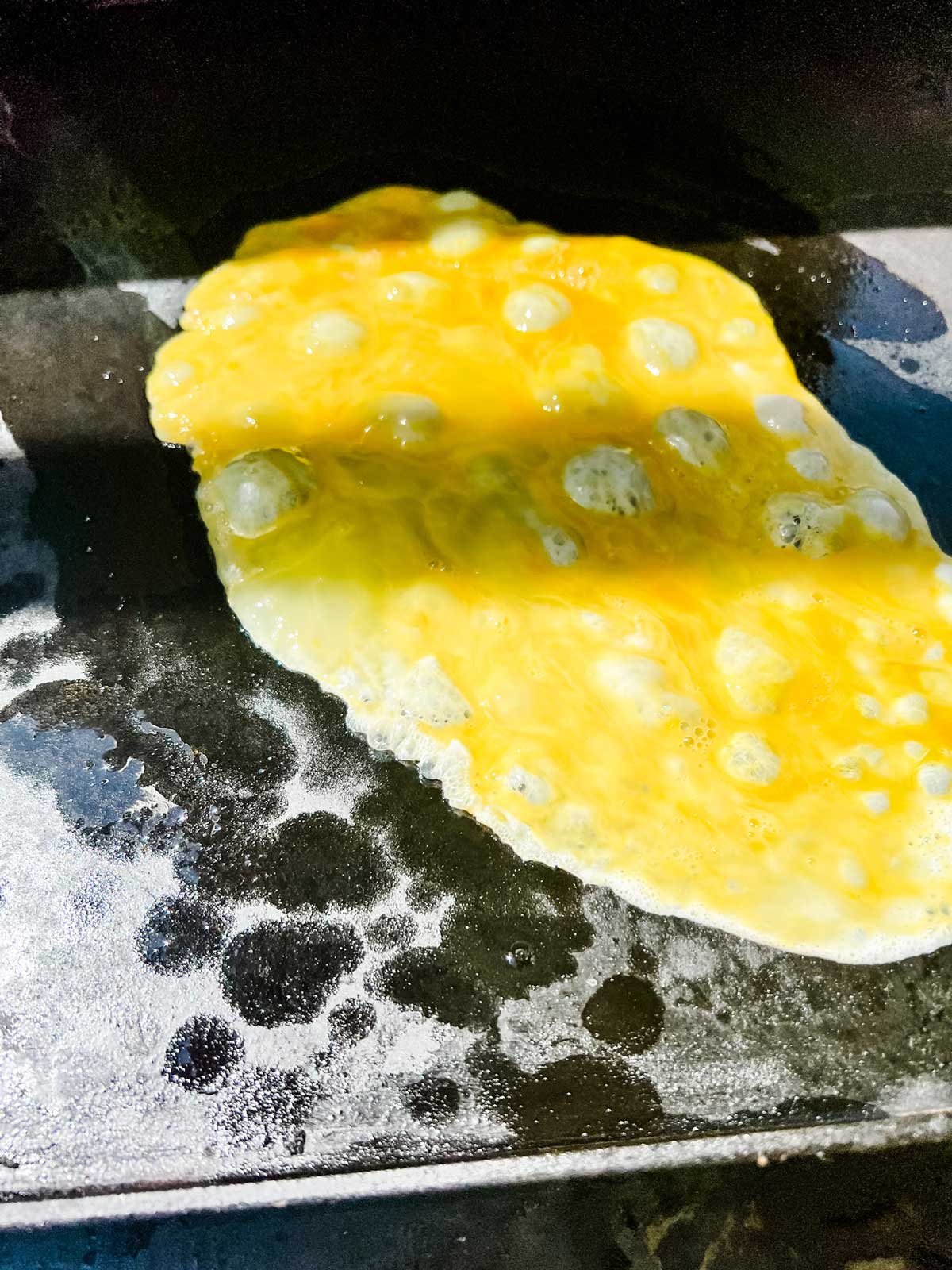 Photo of three eggs just starting to cook on a blackstone griddle.