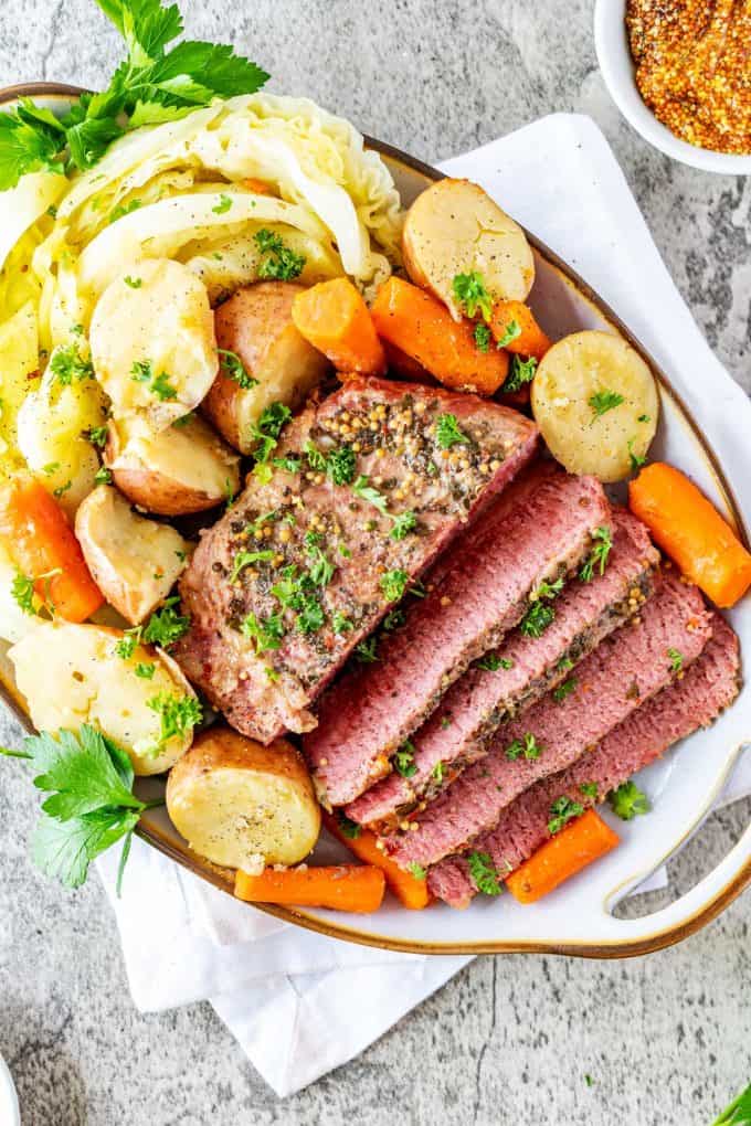 Overhead photo of a platter of Dutch Oven Corned Beef and Cabbage with potatoes, and carrots garnished with parsley.