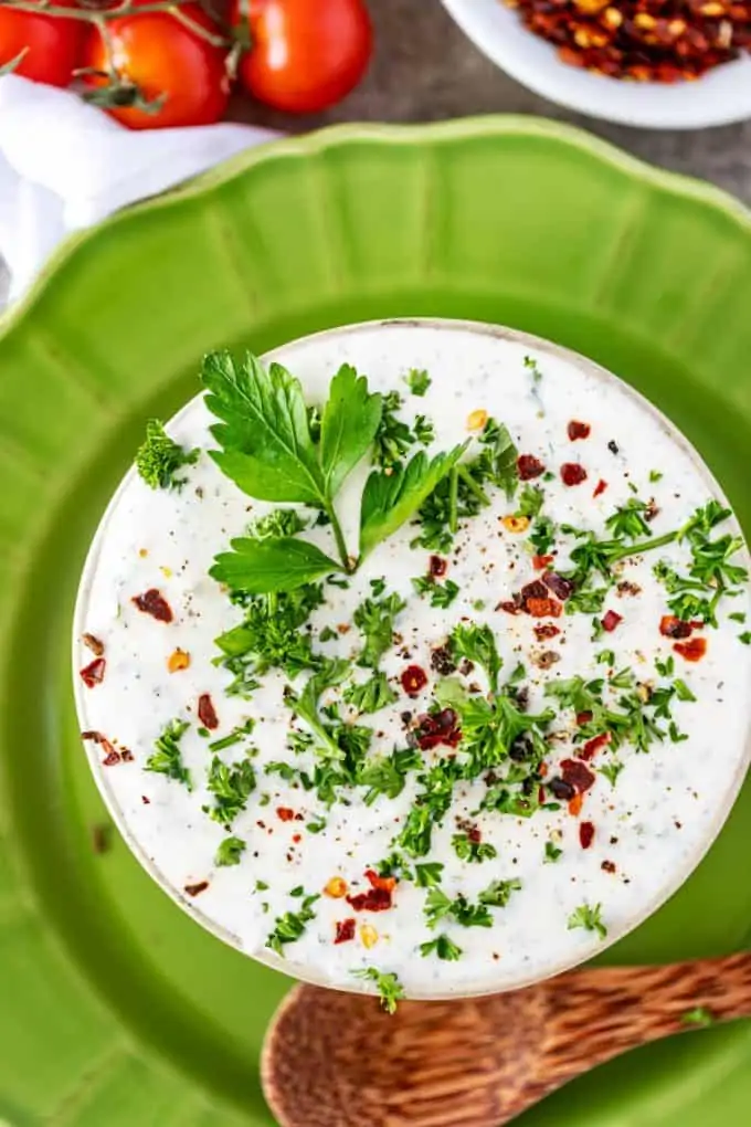 Photo of a small bowl of Greek yogurt ranch dressing sitting on a green plate with a spoon resting on it.