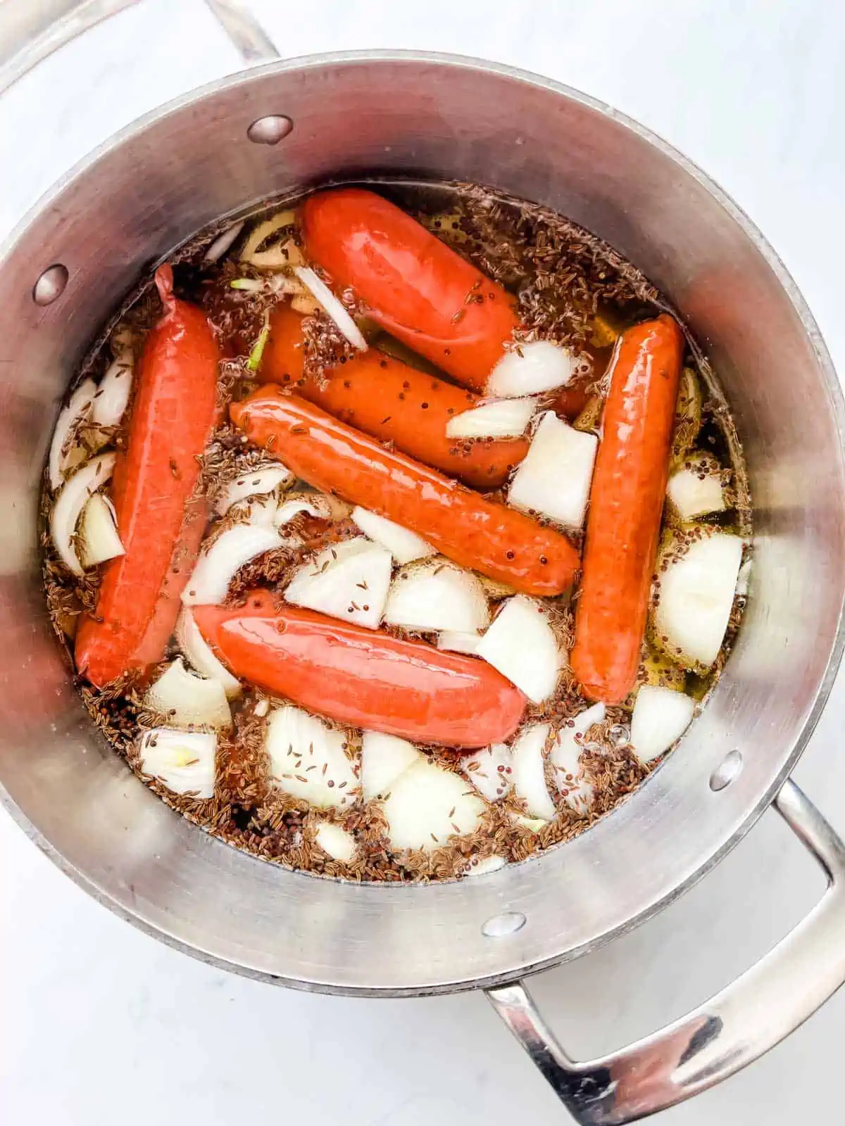 Overhead photo of brats, onions, seasonings, and beer in a large pot.