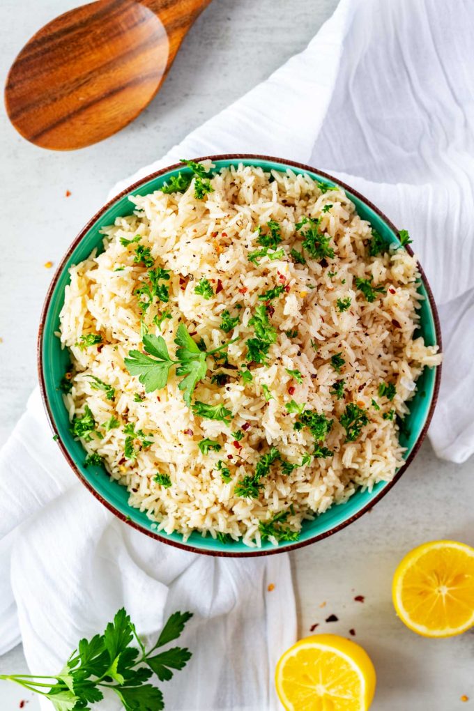 Photo of a bowl of Instant Pot Jasmine Rice with a spoon above it and halved lemon and parsley below it.