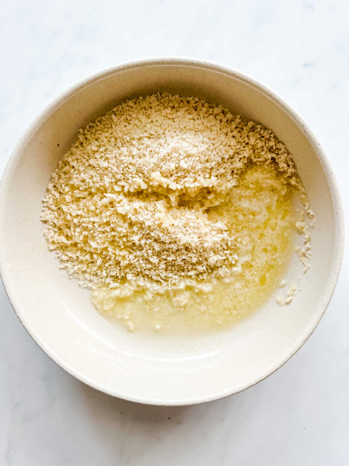 Breadcrumbs and butter being stirred together in a bowl.