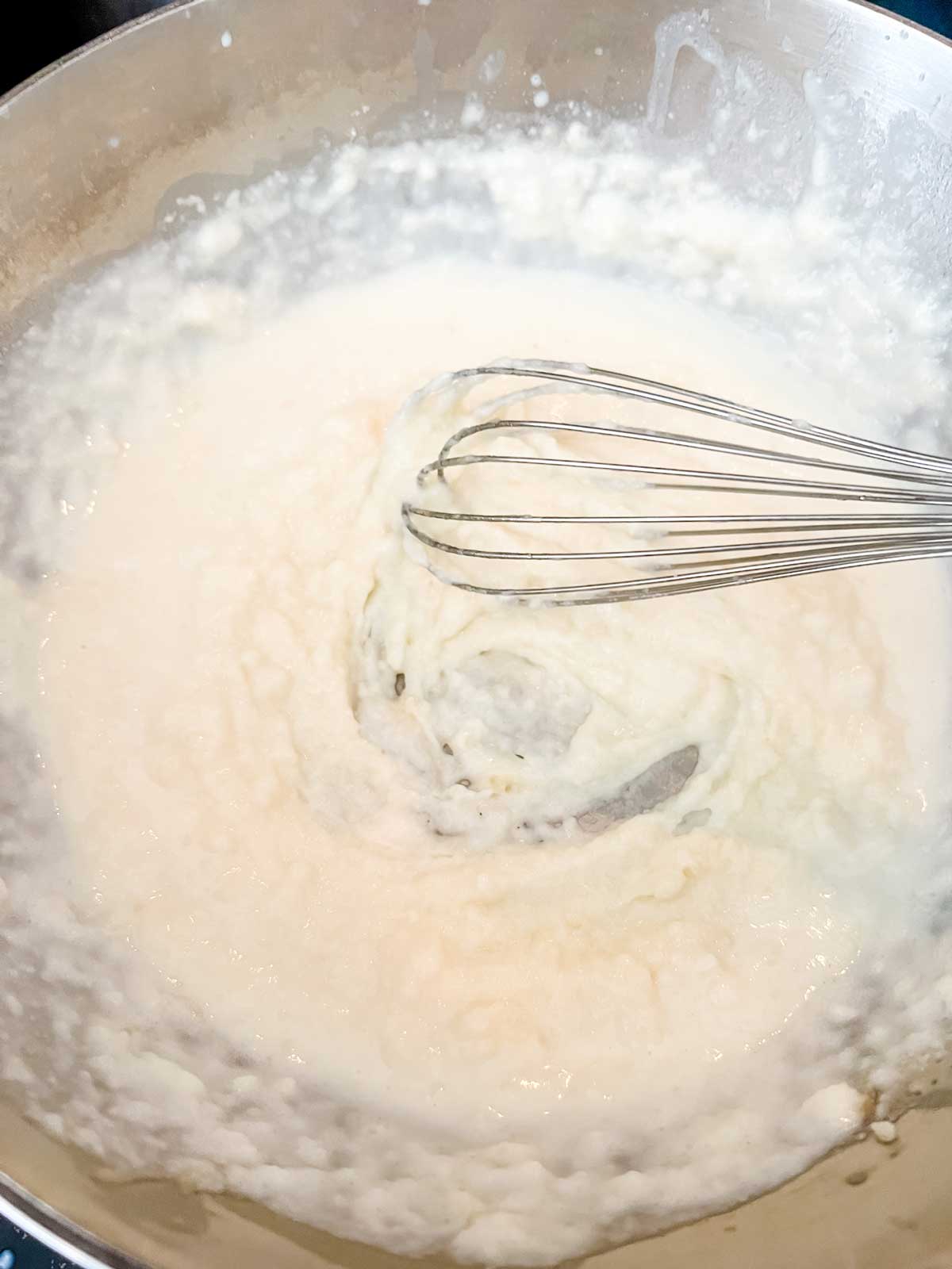Photo of a little bit of milk being added to thin the roux.