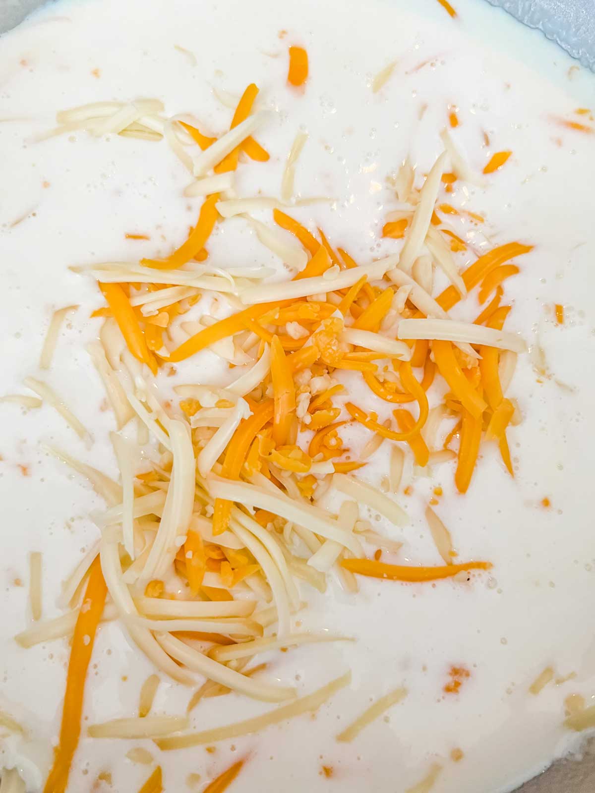 Cheese being added to a cream sauce in a pot.