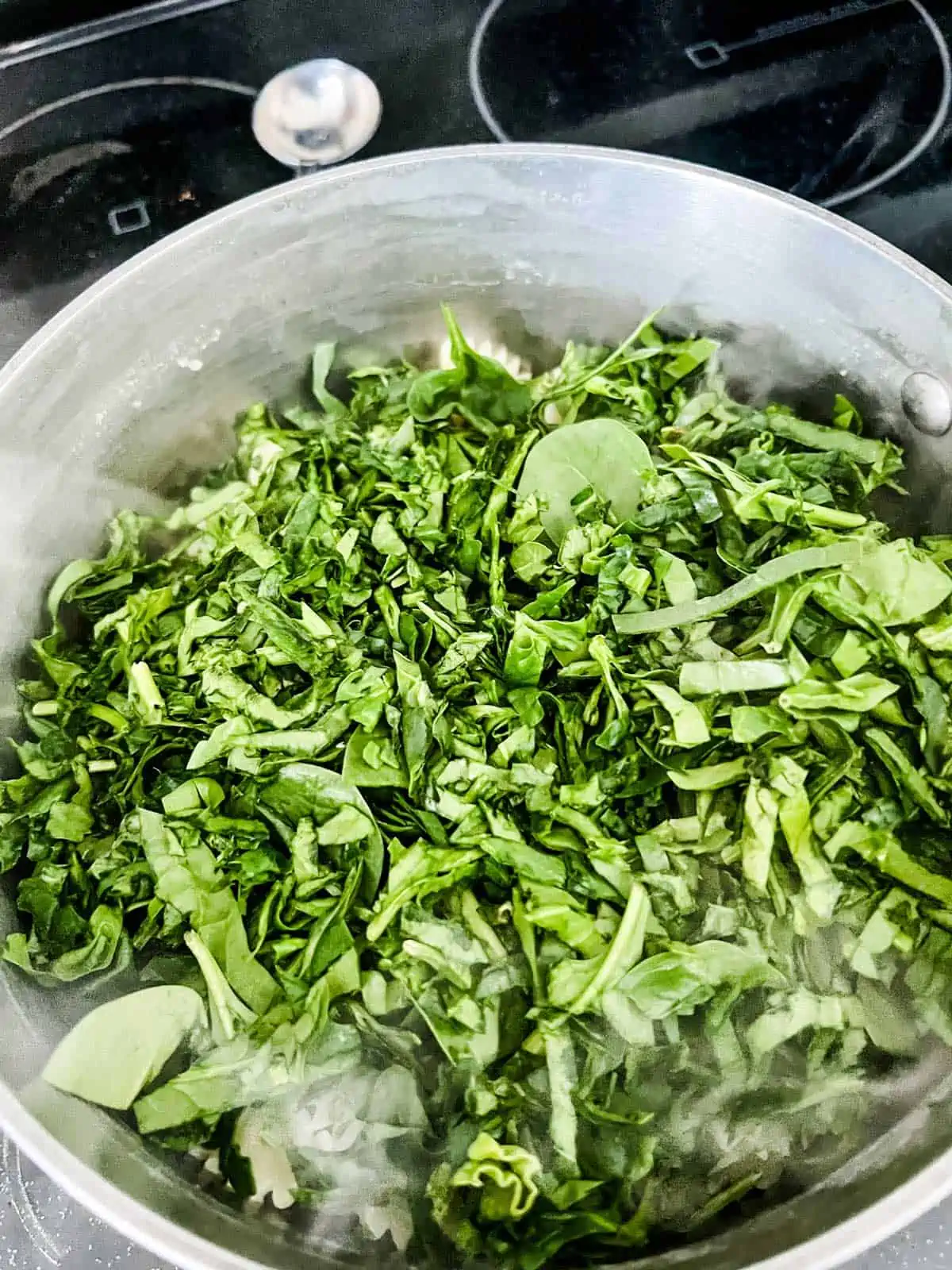 Spinach that has just been added to a saucepan of freshly cooked pasta.