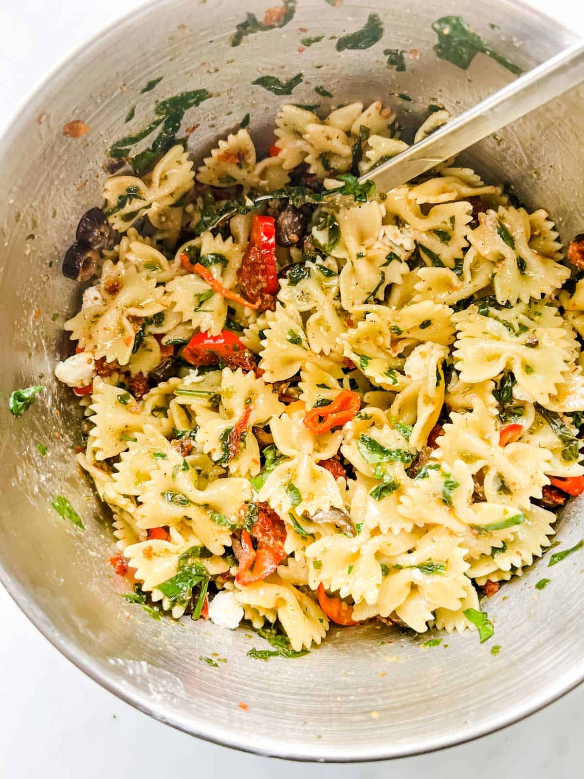 Sun dried tomato pasta salad being mixed together in a large bowl.