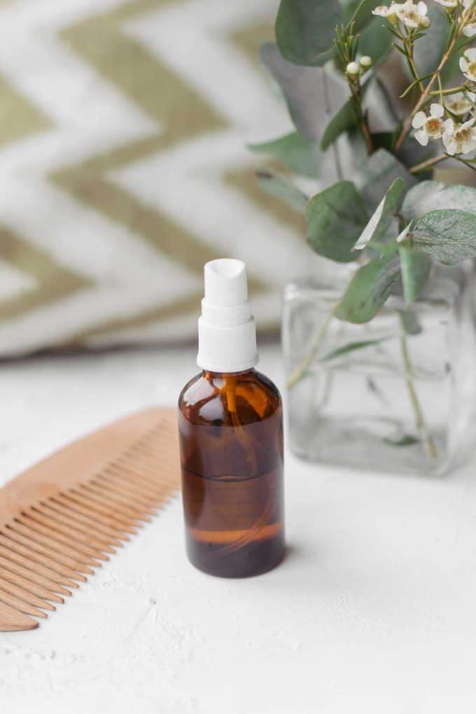 Essential oil spray sitting on a white countertop with a comb besite it.