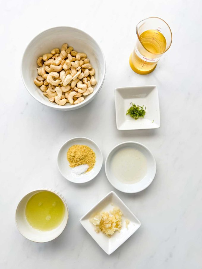 Overhead photo of a cashews, water, garlic, lime juice and zest, nutritional yeast, vinegar, and salt.