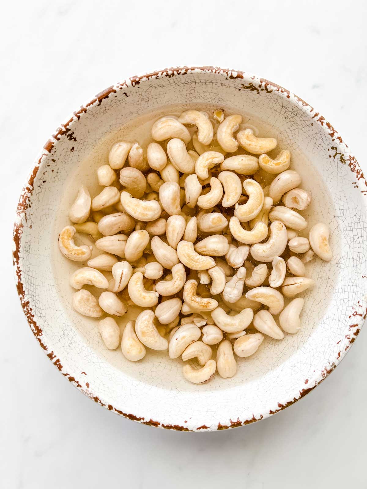Photo of a bowl of raw cashews soaking in water.