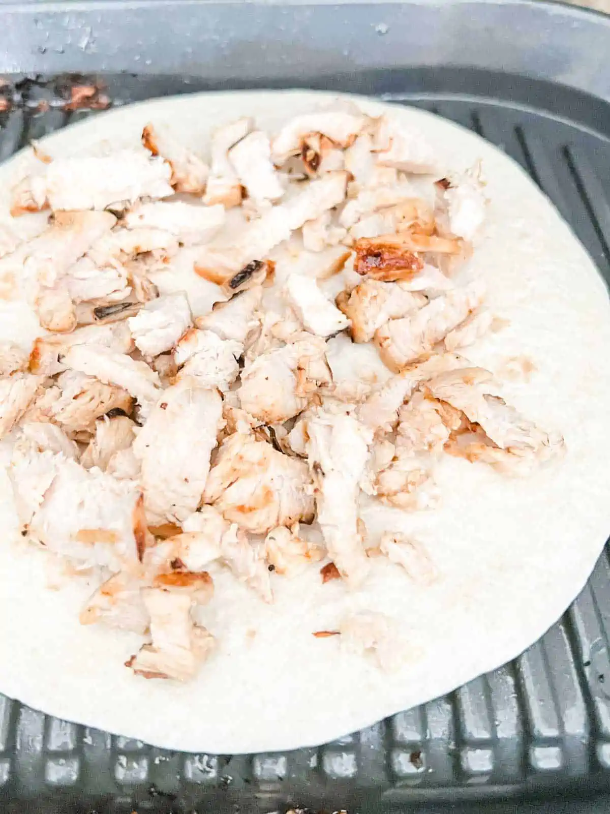 Chopped chicken on a tortilla sitting on a grill.
