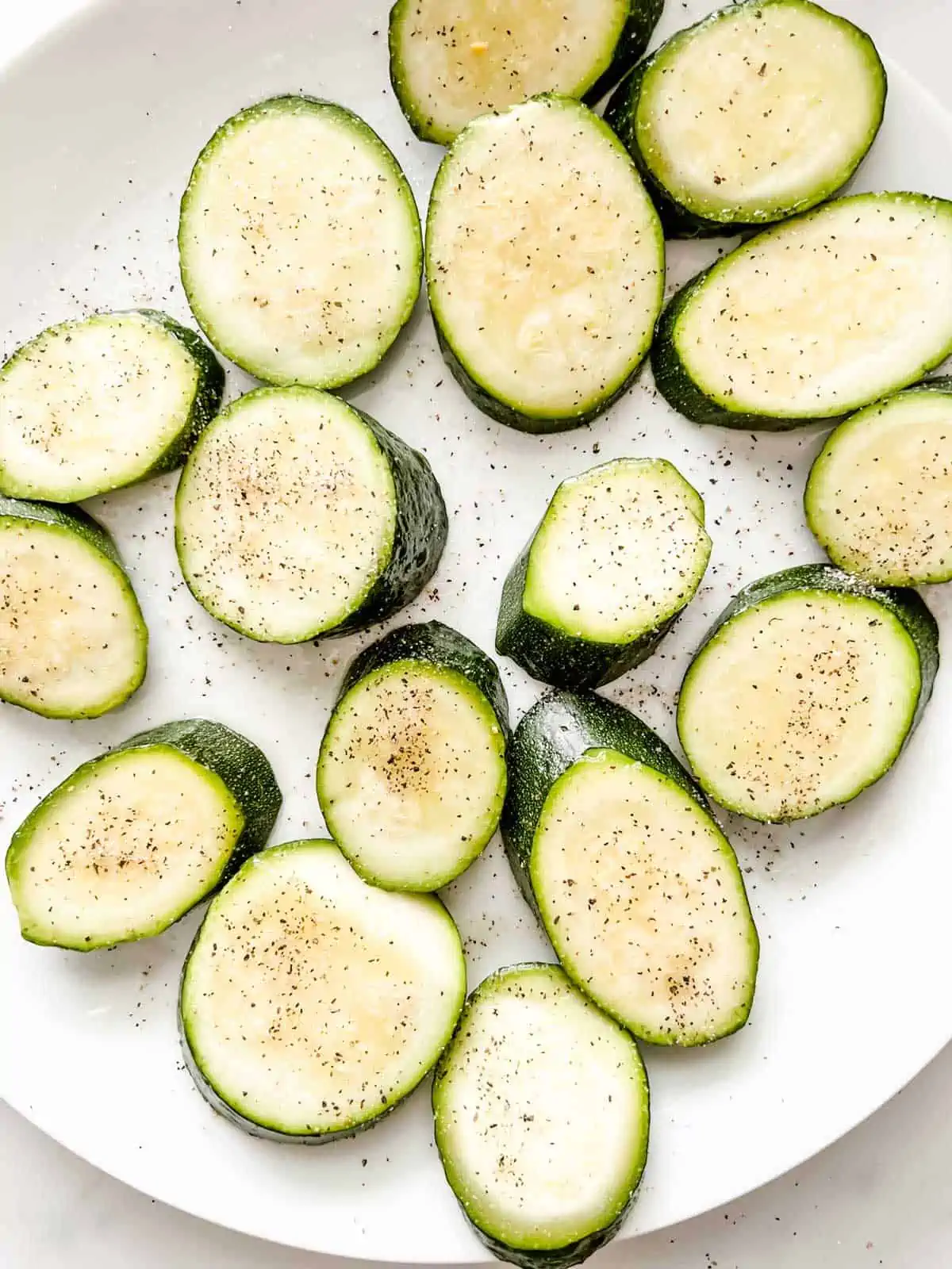 A plate of sliced zucchini that has been seasoned with salt and pepper.