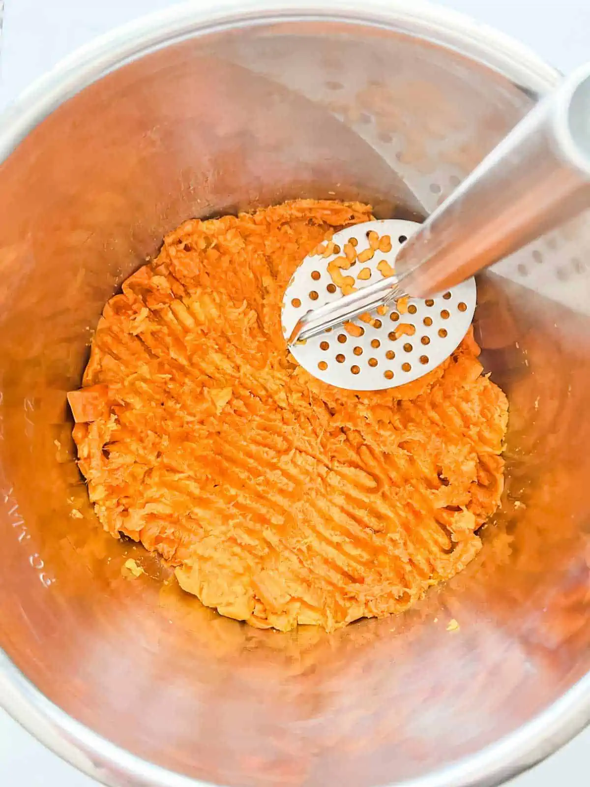A potato masher mashing sweet potatoes in the bowl of an Instant pot.