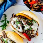 Square photo of a Blackstone Philly Cheesesteak on a white plate garnished with parsley.