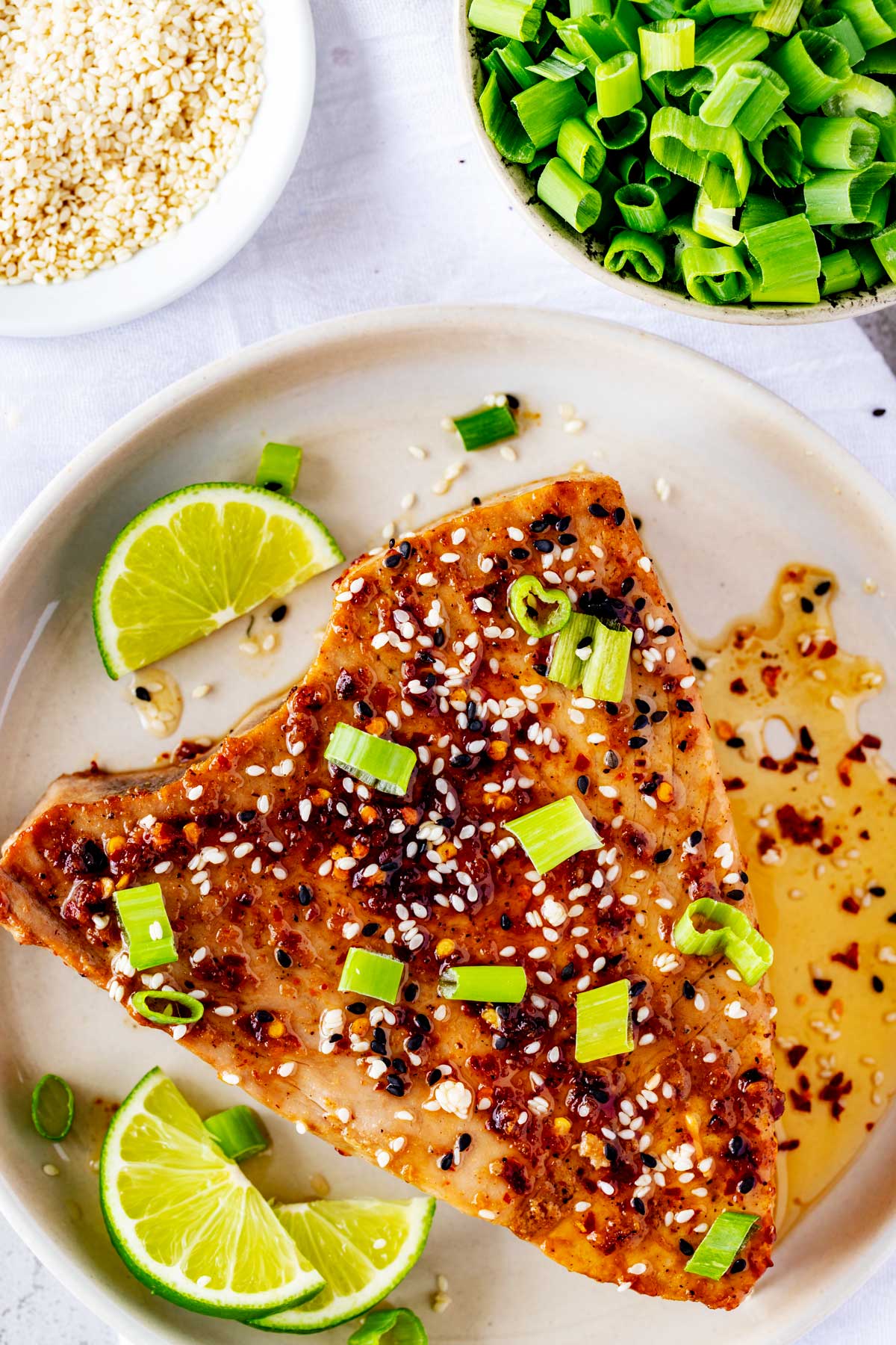 Overhead photo of air fryer tuna steak on a plate with a sesame ginger sauce garnished with scallions and sesame seeds.