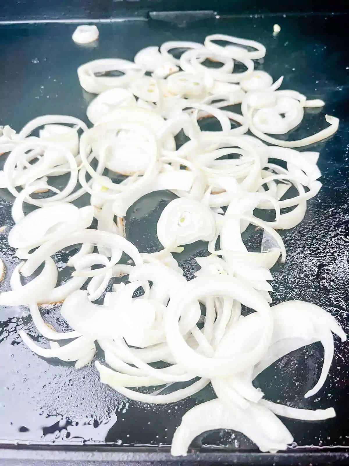 Sliced onions cooking on a griddle.