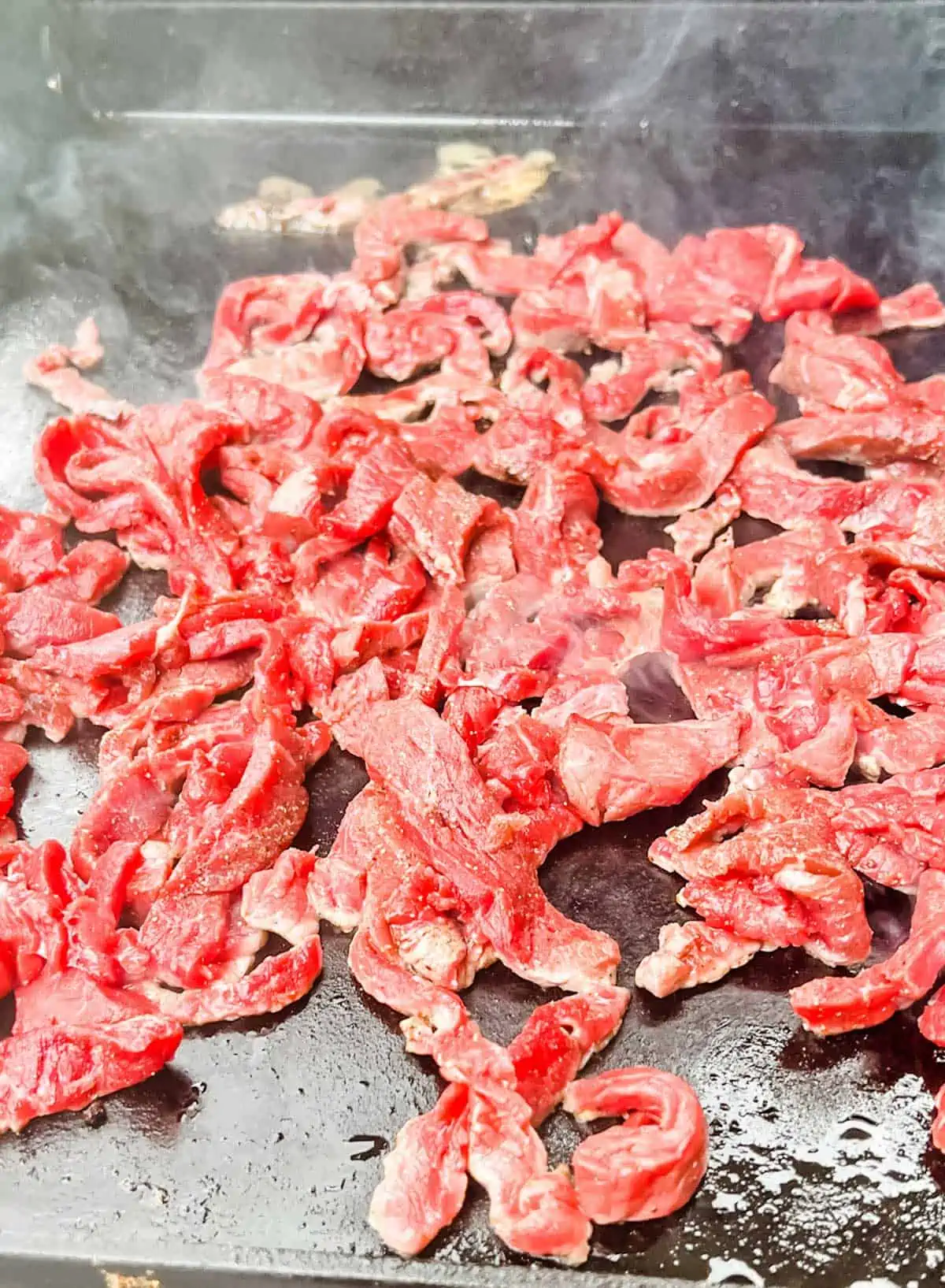 Thinly sliced steak cooking on a Blackstone griddle.