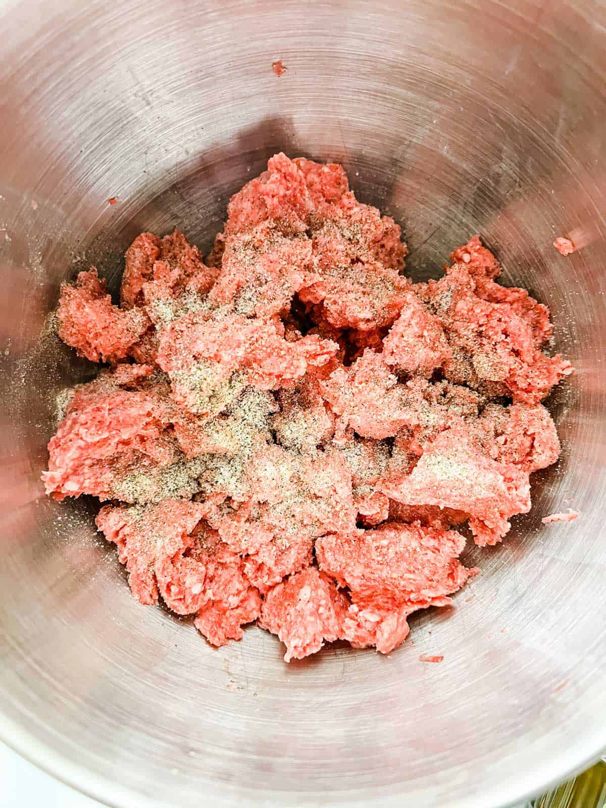 Photo of ground beef being seasoned in a large bowl.