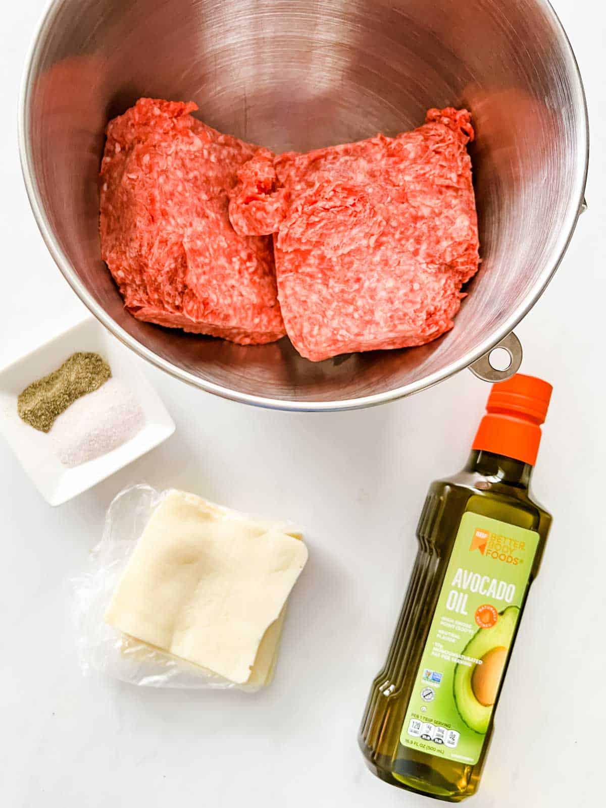Overhead photo of a bowl of ground beef, seasonings, sliced cheese, and avocado oil.