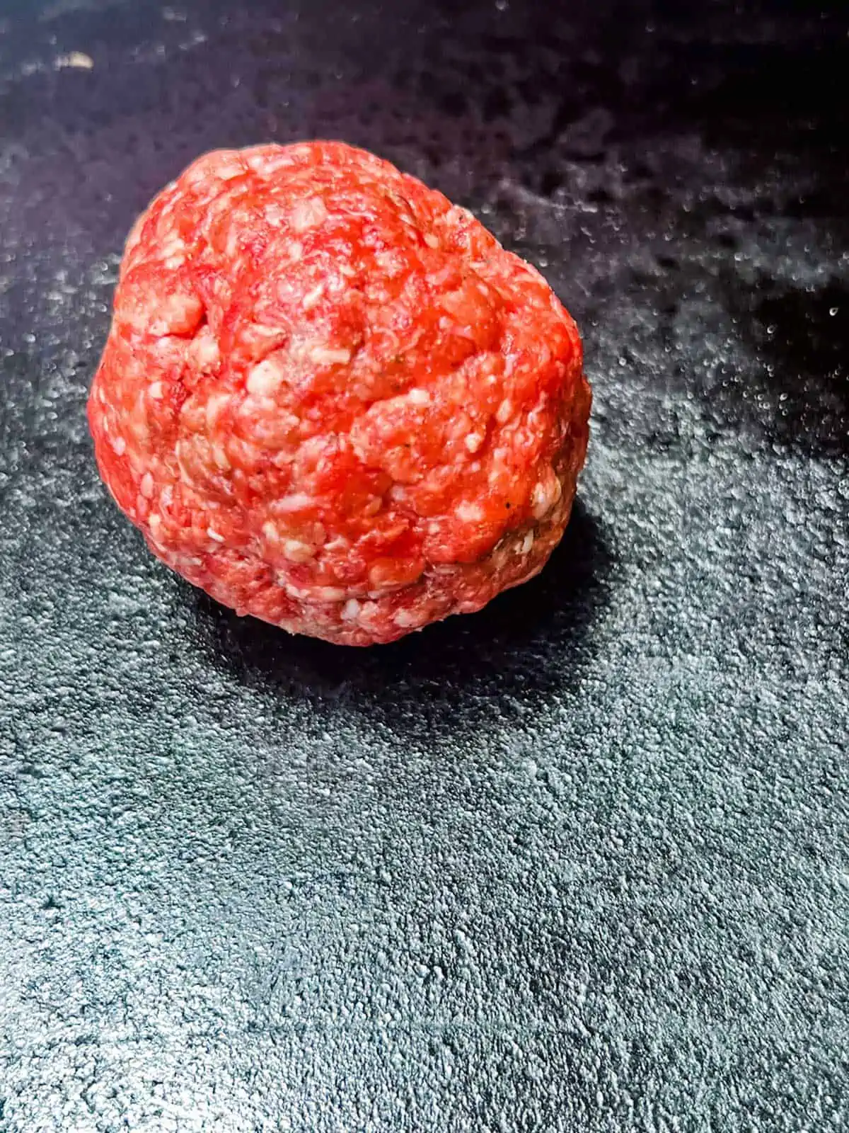 Photo of a ball or ground beef on a Blackstone griddle.