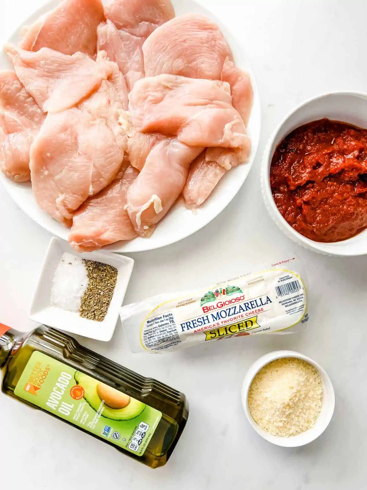 Overhead photo of chicken breast, marinara, fresh mozzarella, parmesan, seasonings, and avocado oil.