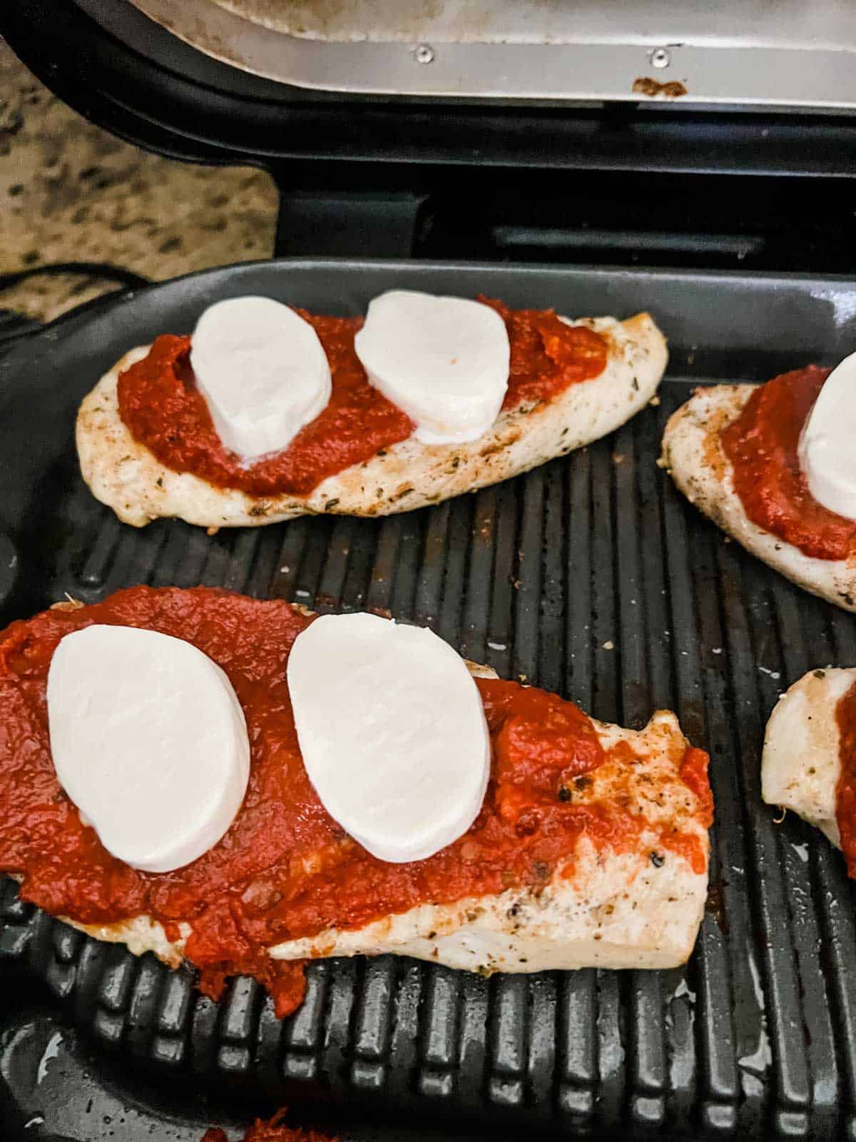 Photo of grilled chicken with marinara and fresh mozzarella on top of it.