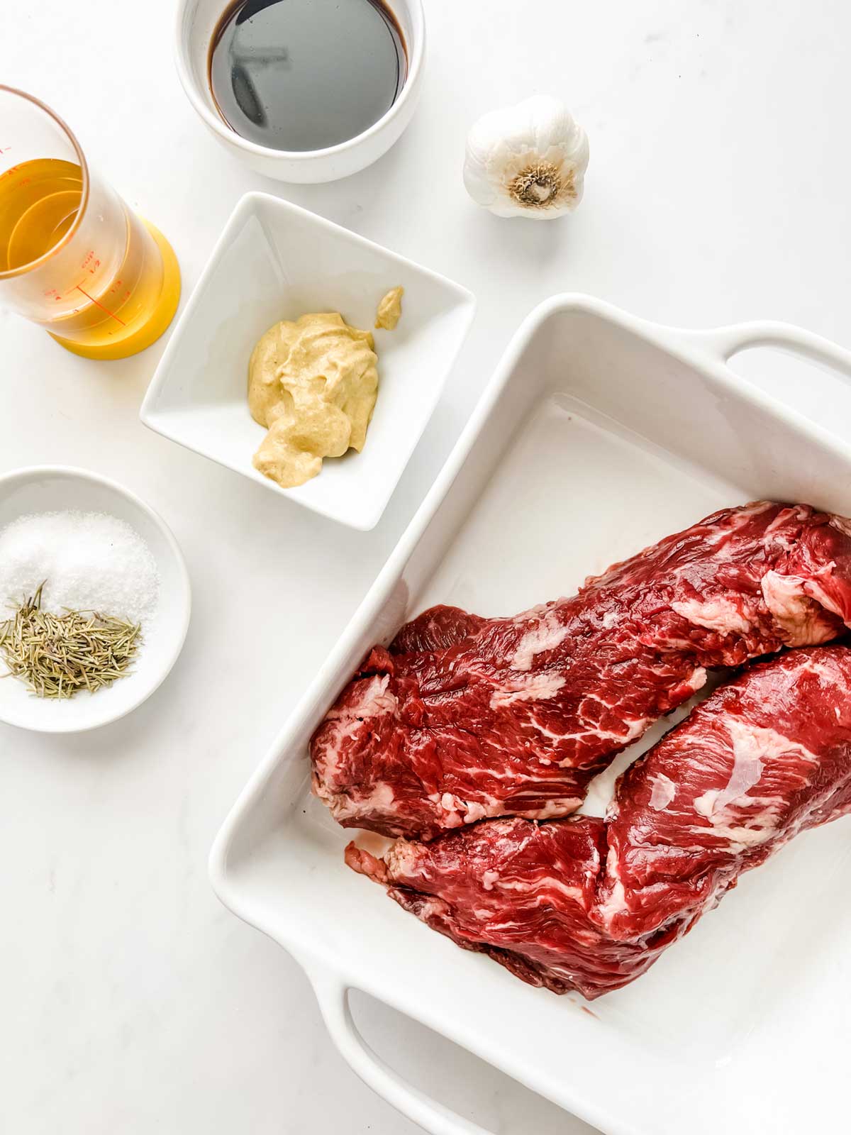 Overhead photo of hanger steak in a shallow dish, dijon mustard, soy sauce, oil, seasonings, and garlic.
