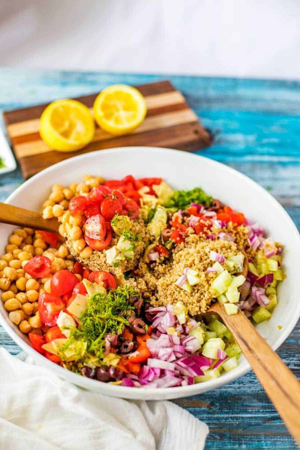 Mediterranean quinoa salad being tossed in a large white bowl.