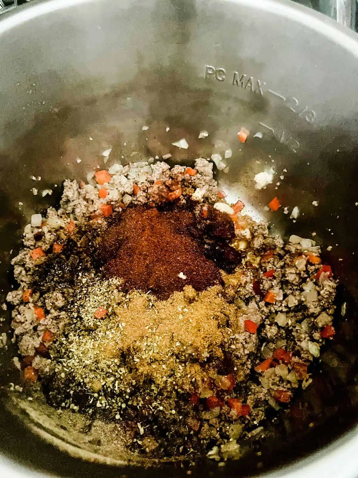 Seasonings that have been dumped on top of ground beef, onion, and red pepper in an Instant Pot.