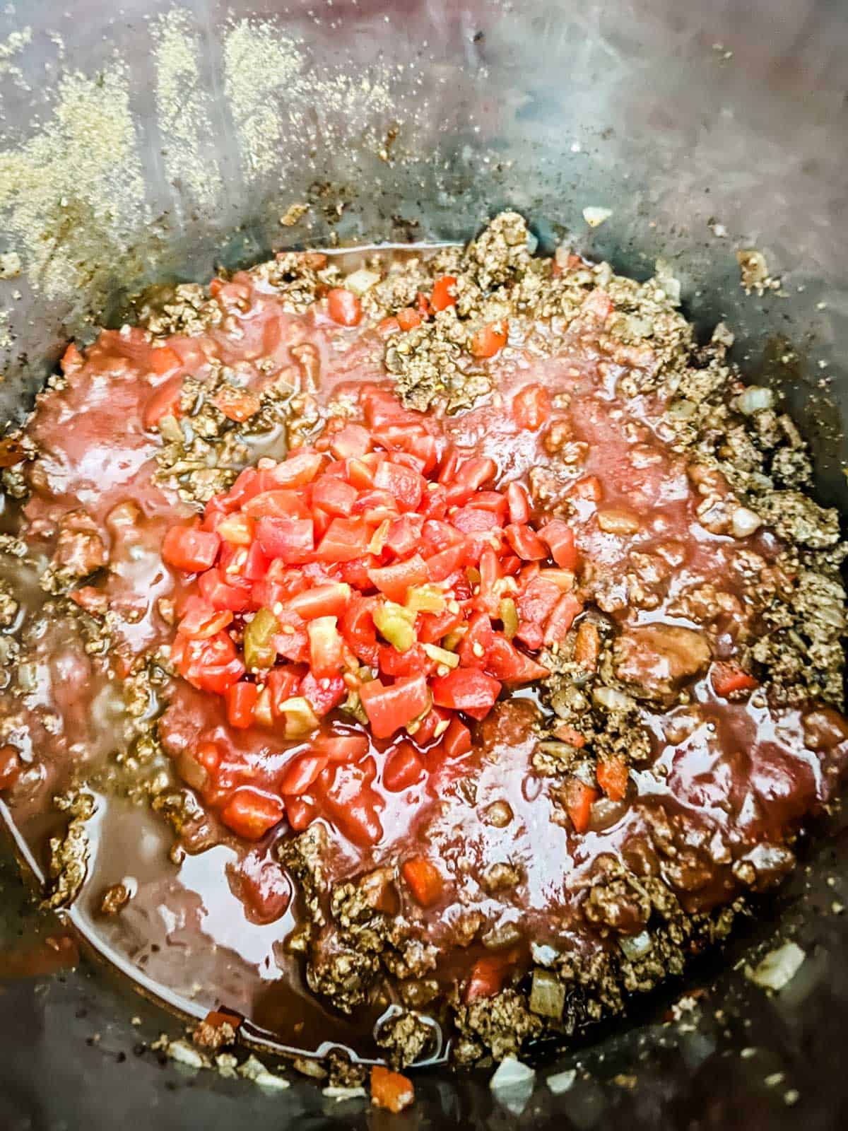 Tomatos and broth on top of seasoned ground beef and vegetables in an Instant Pot.