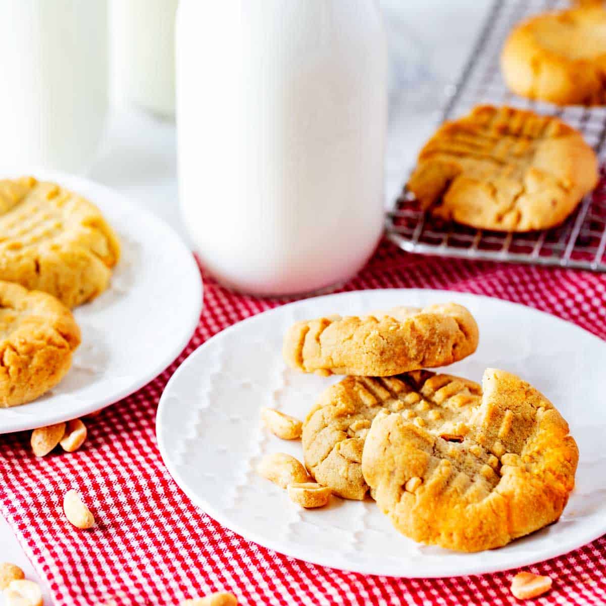 Square photo of two plates of air fryer peanut butter cookies with milk jars behind them and a cooling rack.