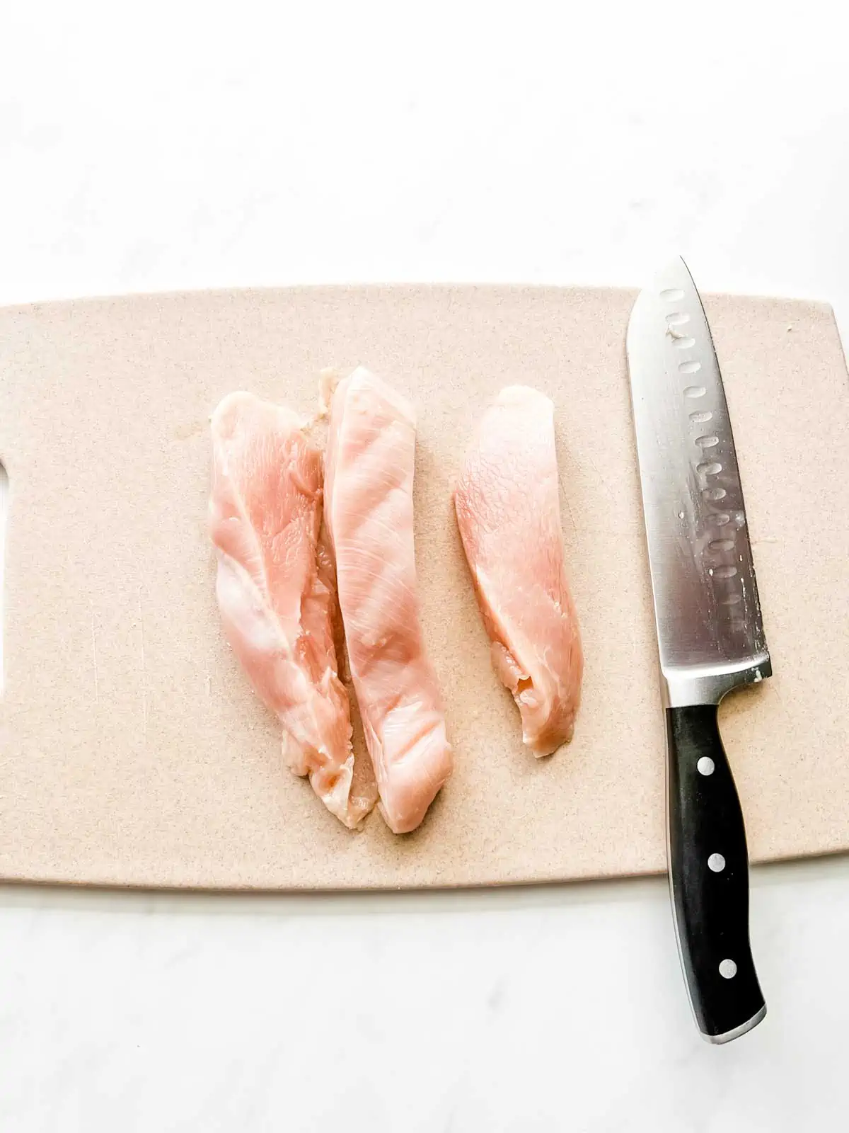 Photo of boneless skinless chicken breast on a cutting board.
