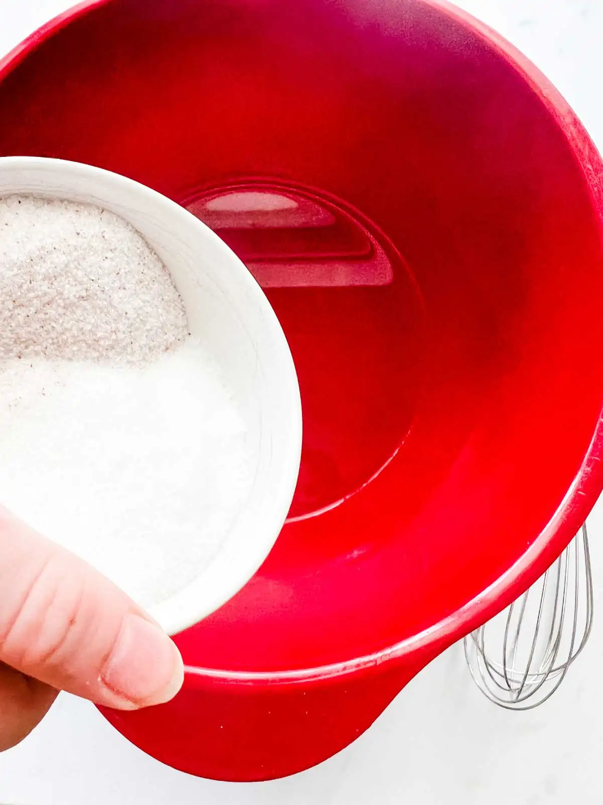 Photo of salt and sugar being poured into a red bowl of water.