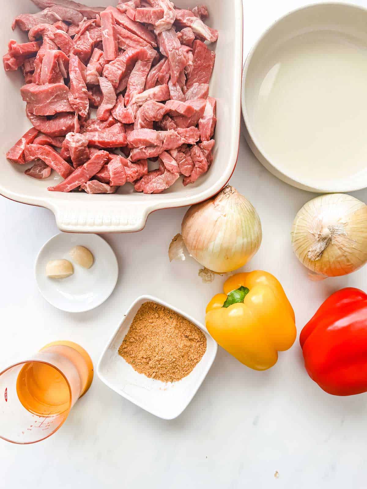 Overhead photo of sliced steak, onion, peppers, lime juice, oil, garlic and seasonings.
