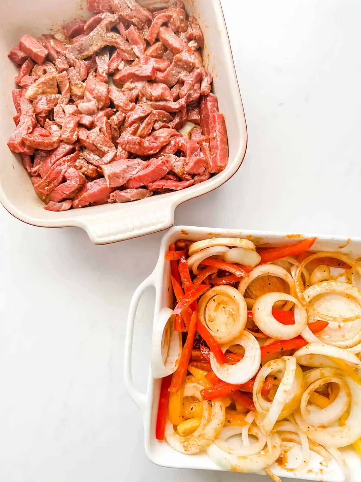 A shallow dish of sliced steak in marinade and sliced onions and peppers.