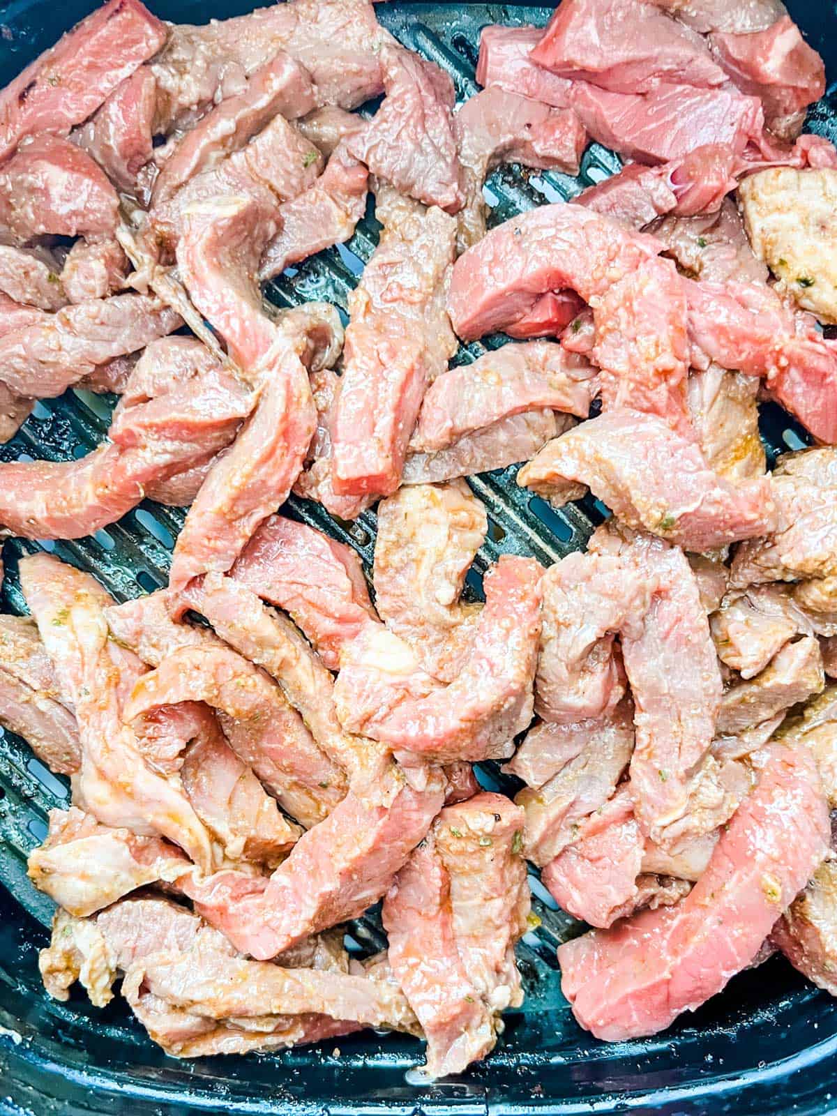 Photo of steak fajita meat cooking in an air fryer.