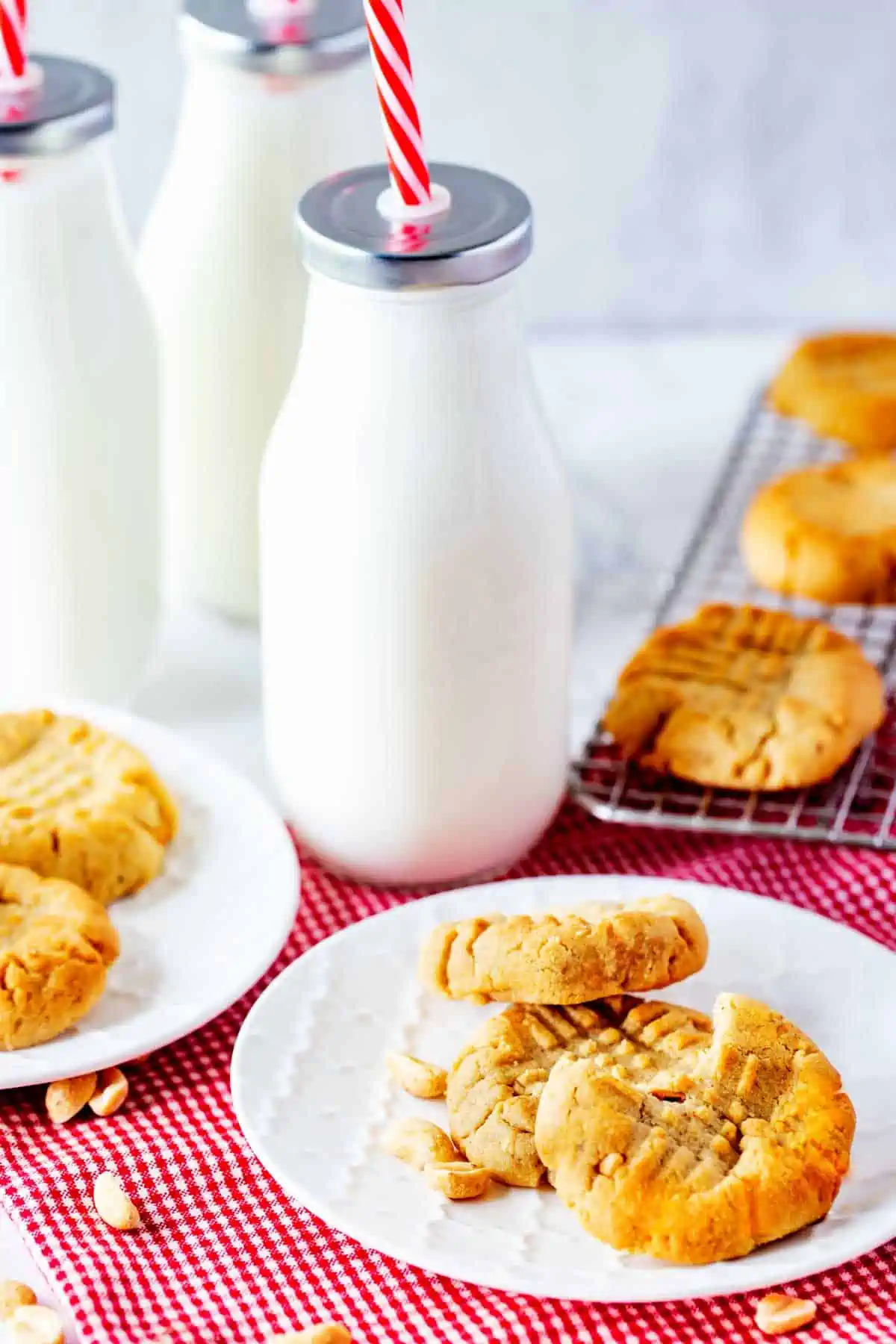 Photo of two plates of air fryer peanut butter cookies with milk jars behind them and a cooling rack.