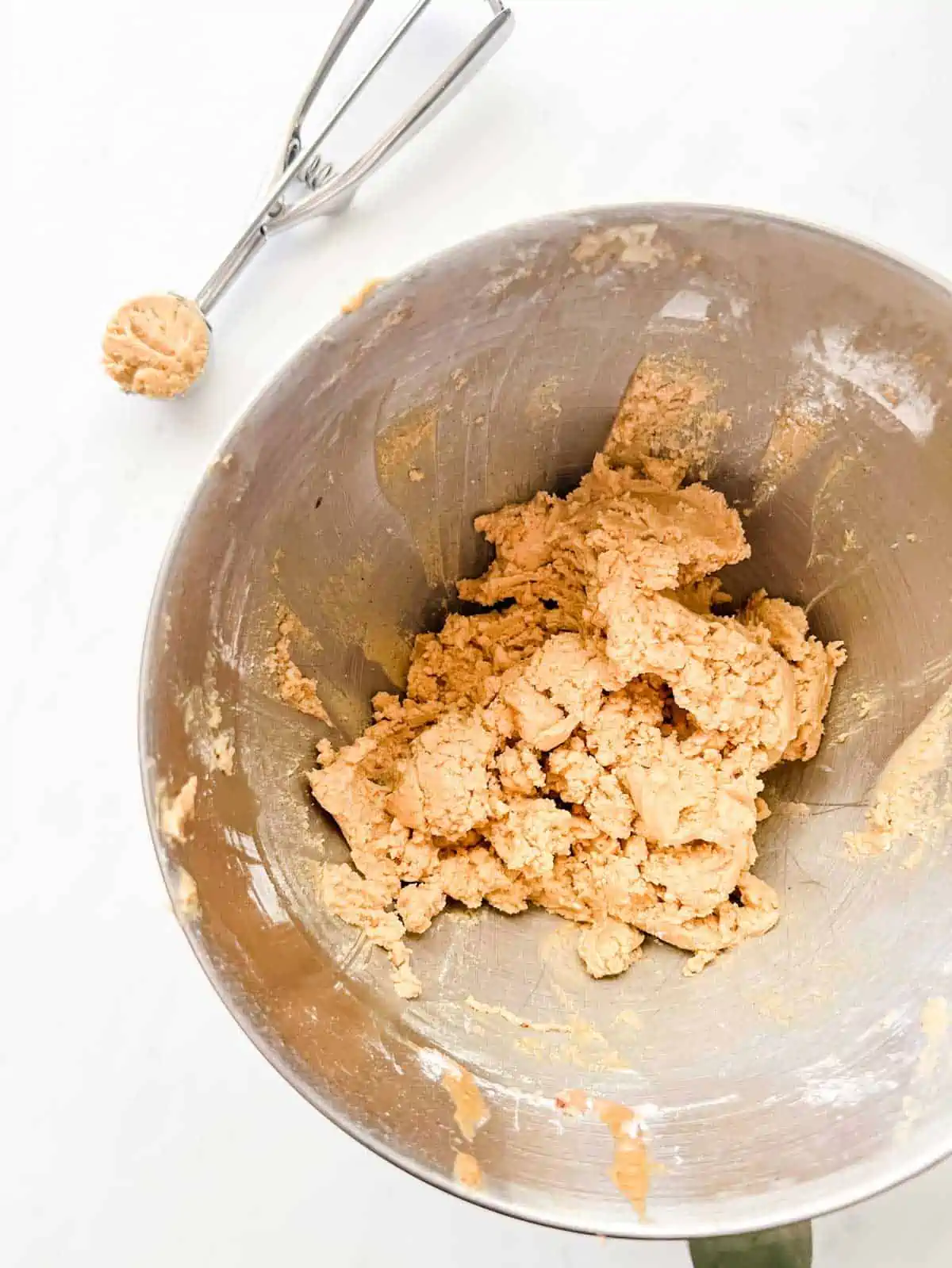 The bowl of a stand mixer with air fryer peanut butter cookies in it and a cookie scoop next to it.