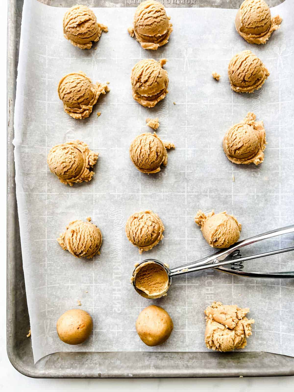 Photo of a parchment lined sheet pan with peanut butter cookies being scooped and rolled onto it.