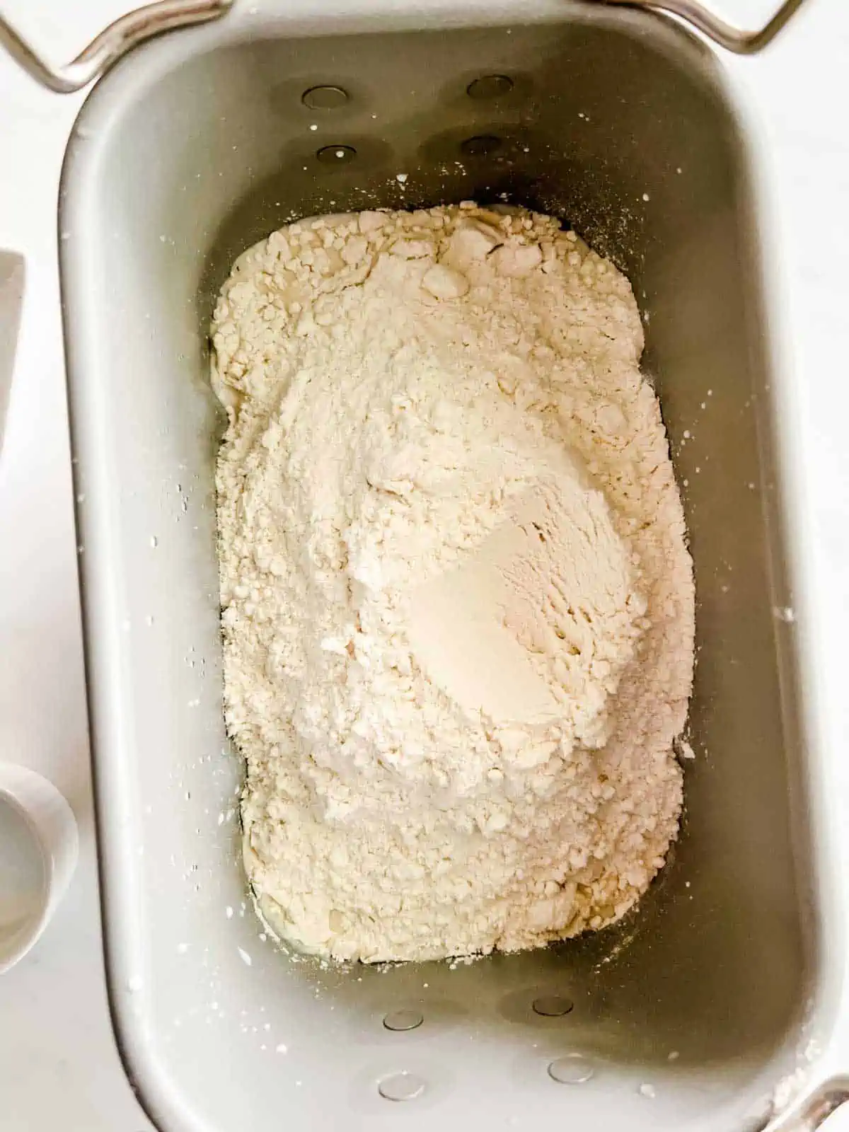 Photo of a bread machine that has had flour added to it on top of wet ingredients.