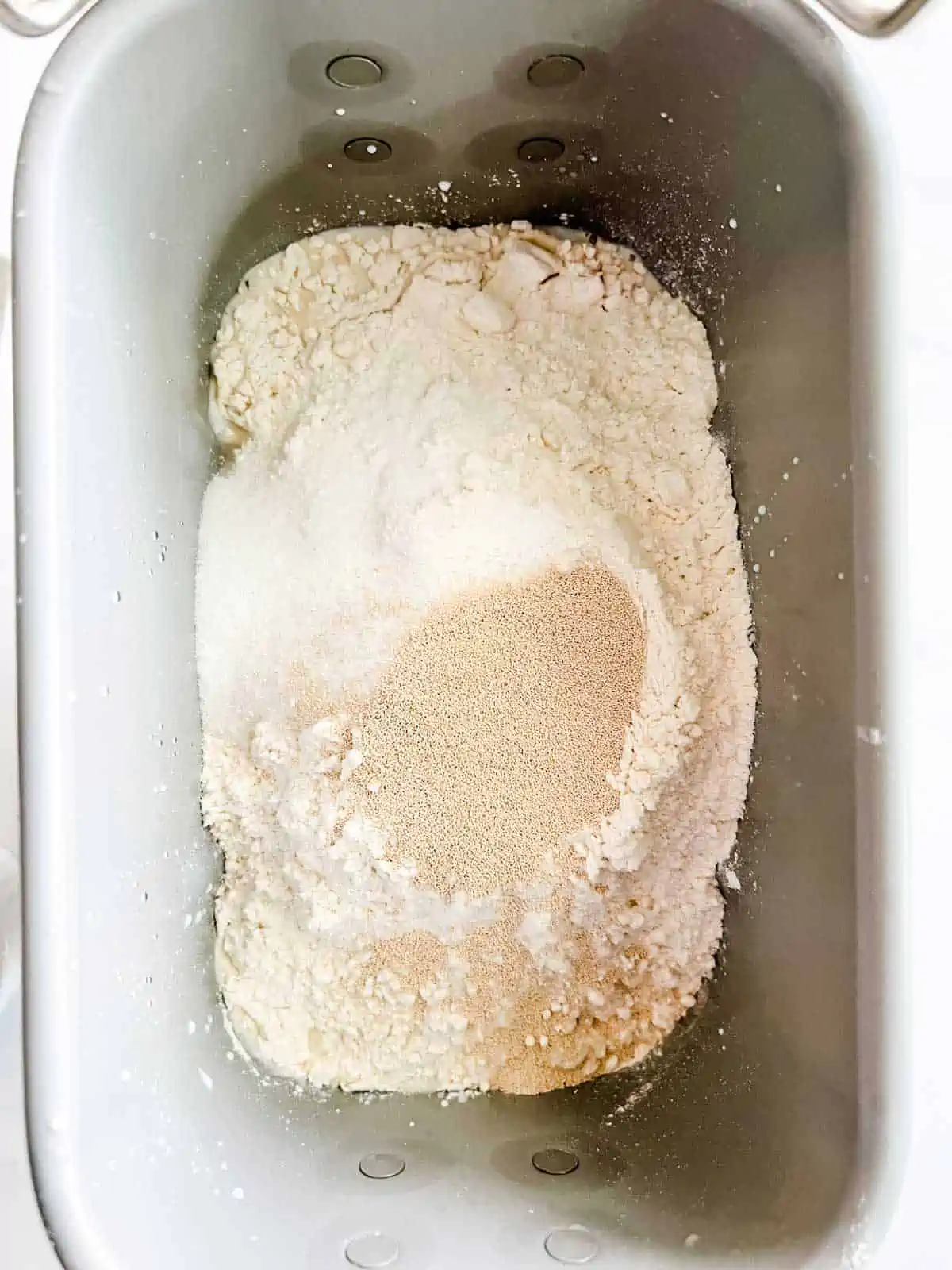Photo of a bread machine that has had yeast and sugar added on top of the flour and wet ingredients.