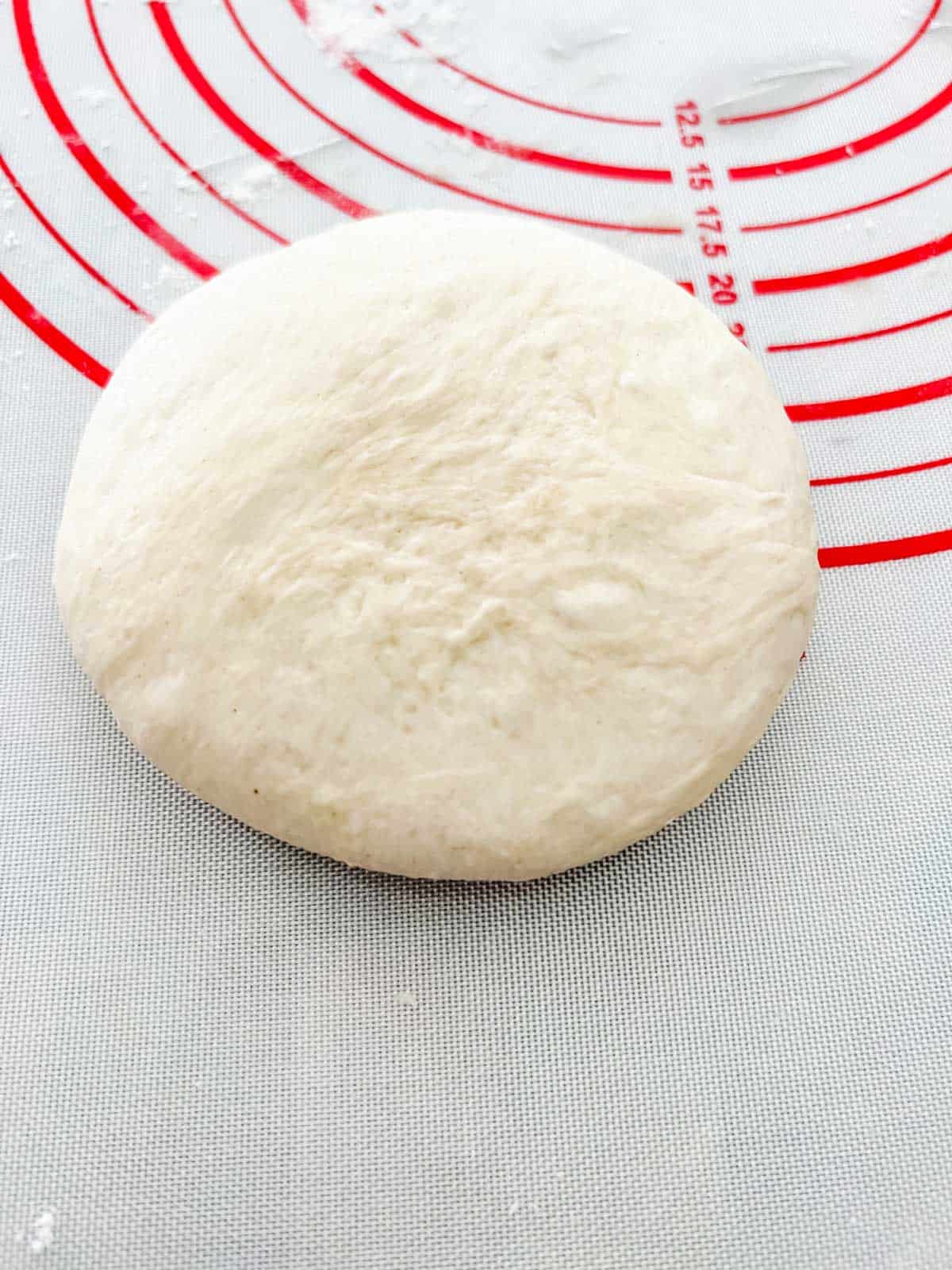 Photo of a ball of burger bun dough that has been flattened.