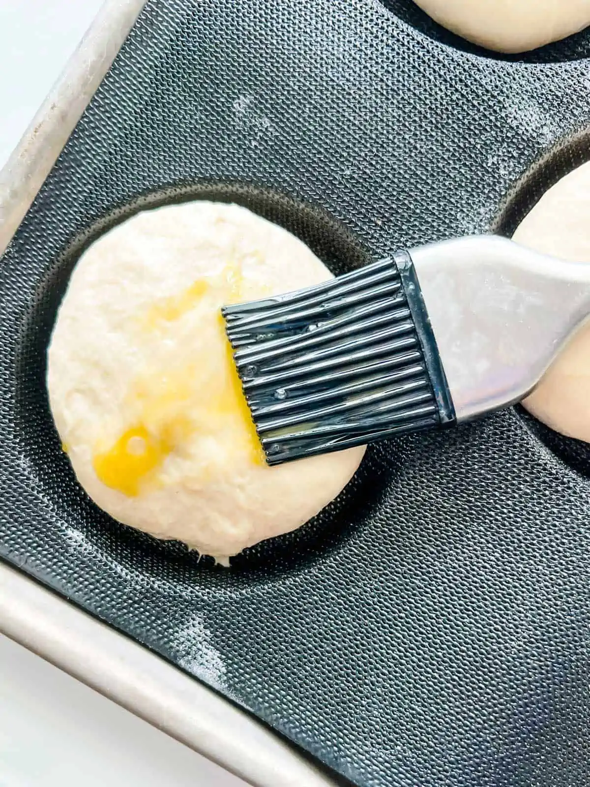 Photo of a burger bun being brushed with an egg wash.