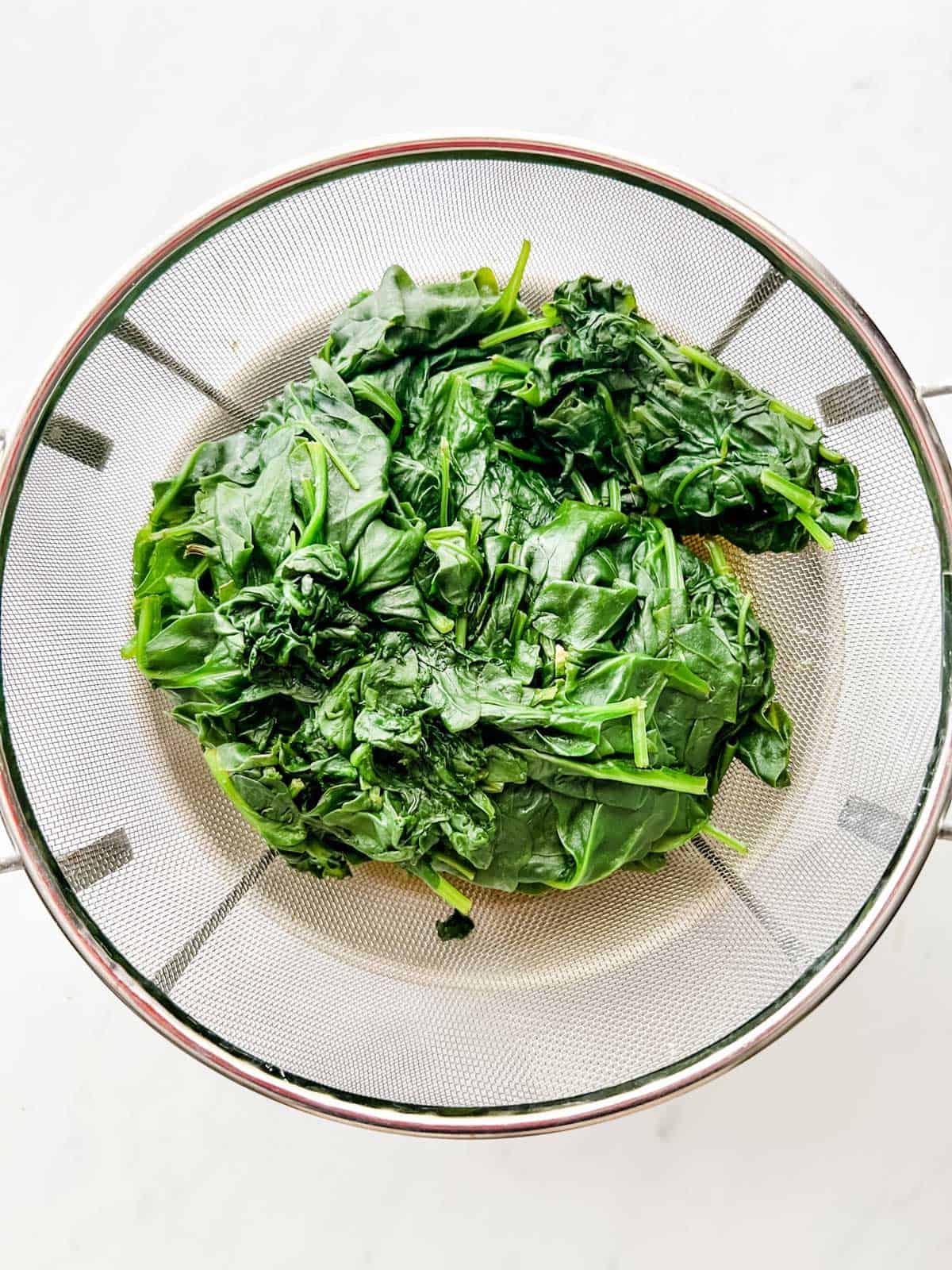 Cooked spinach in a colander.