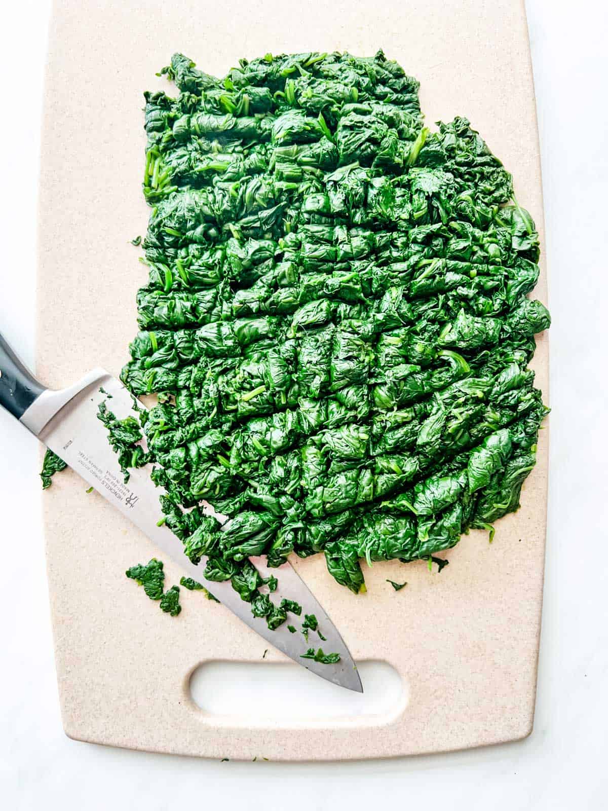 Cooked spinach being chopped on a cutting board.