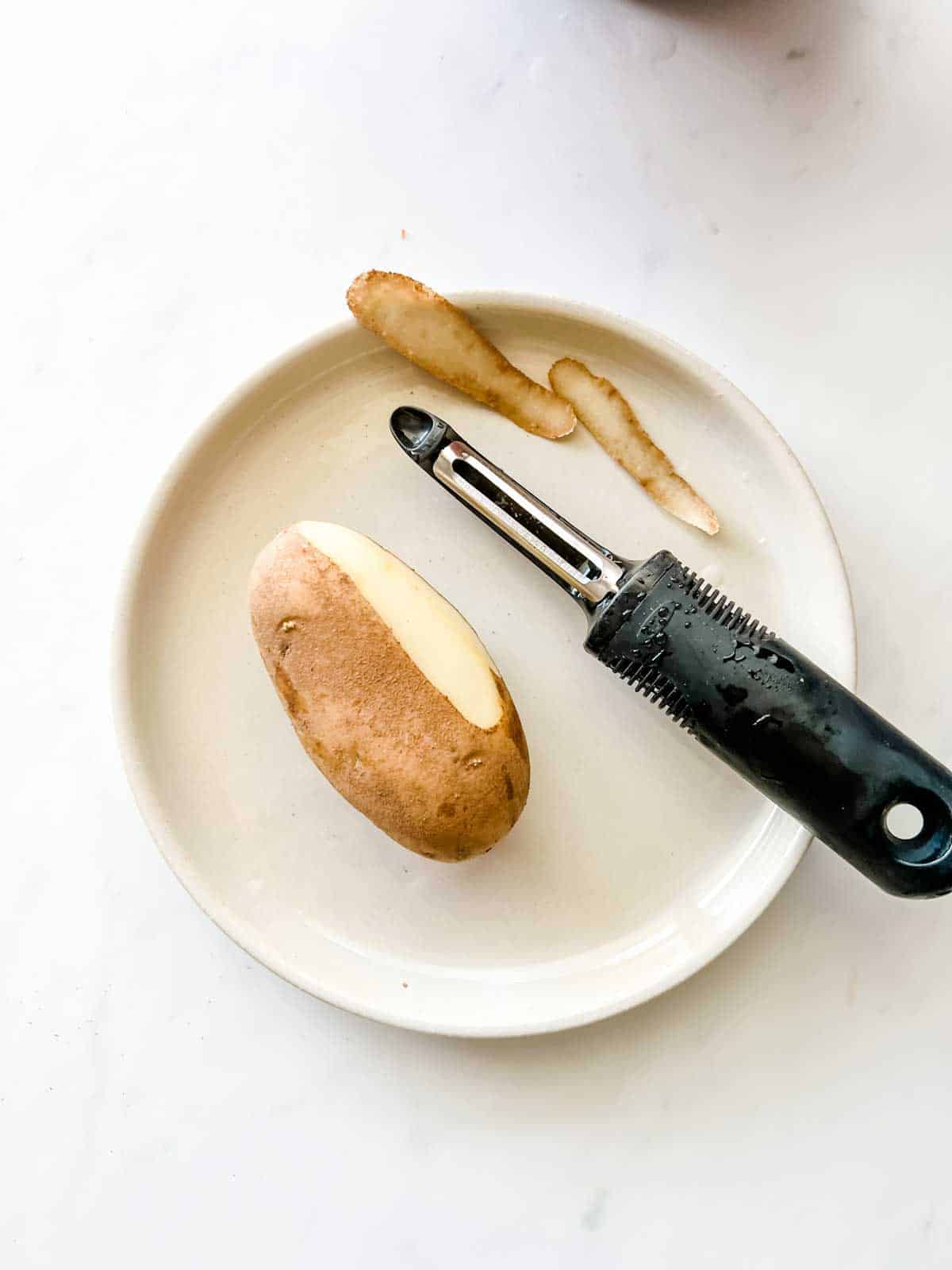 Photo of a potato partially peeled and a potato peeler.