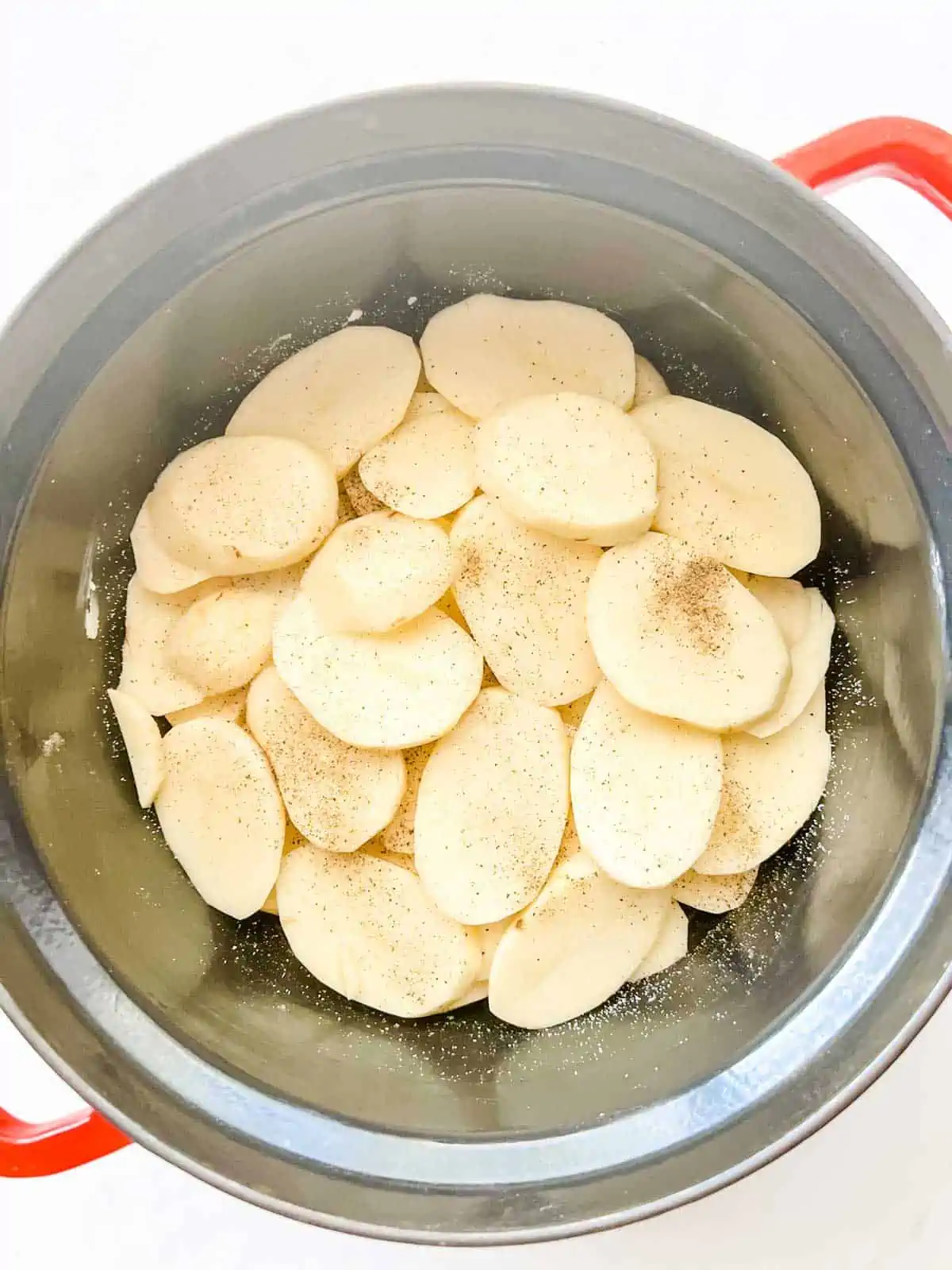 Sliced potatoes in the bottom of a slow cooker.