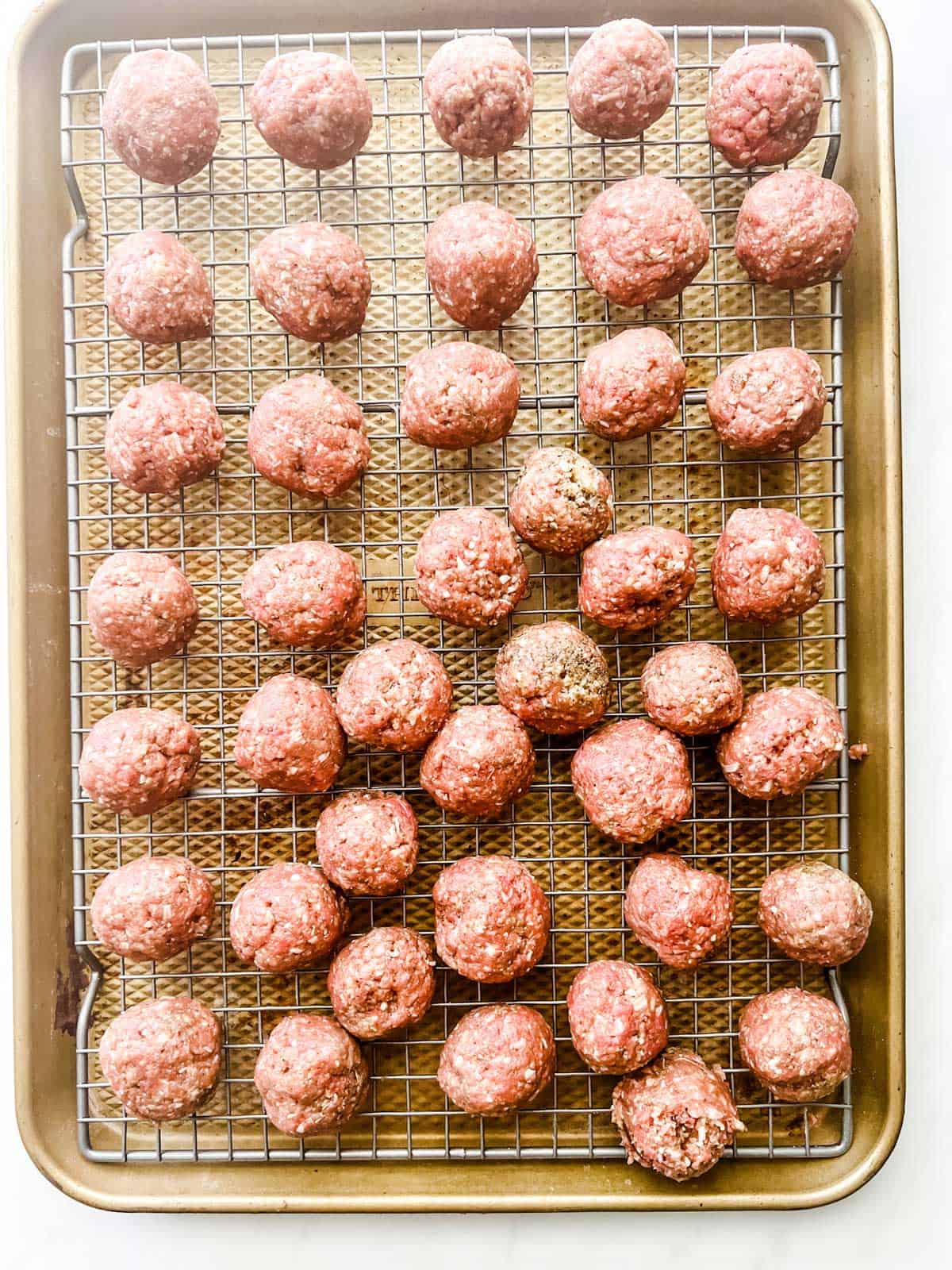 Photo of meatballs on a wire rack set on top of a baking sheet.