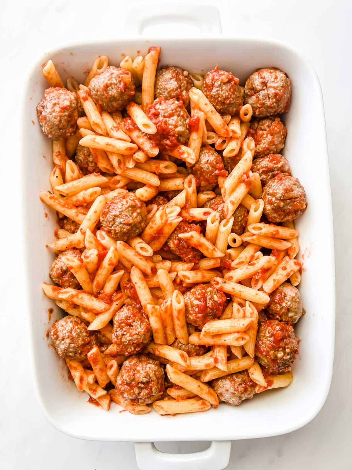 Photo of meatballs and penne pasta tossed with marinara in a casserole dish.