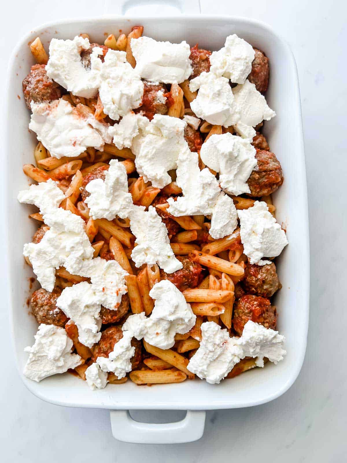 Photo of meatballs, marinara, and penne pasta topped with ricotta cheese.