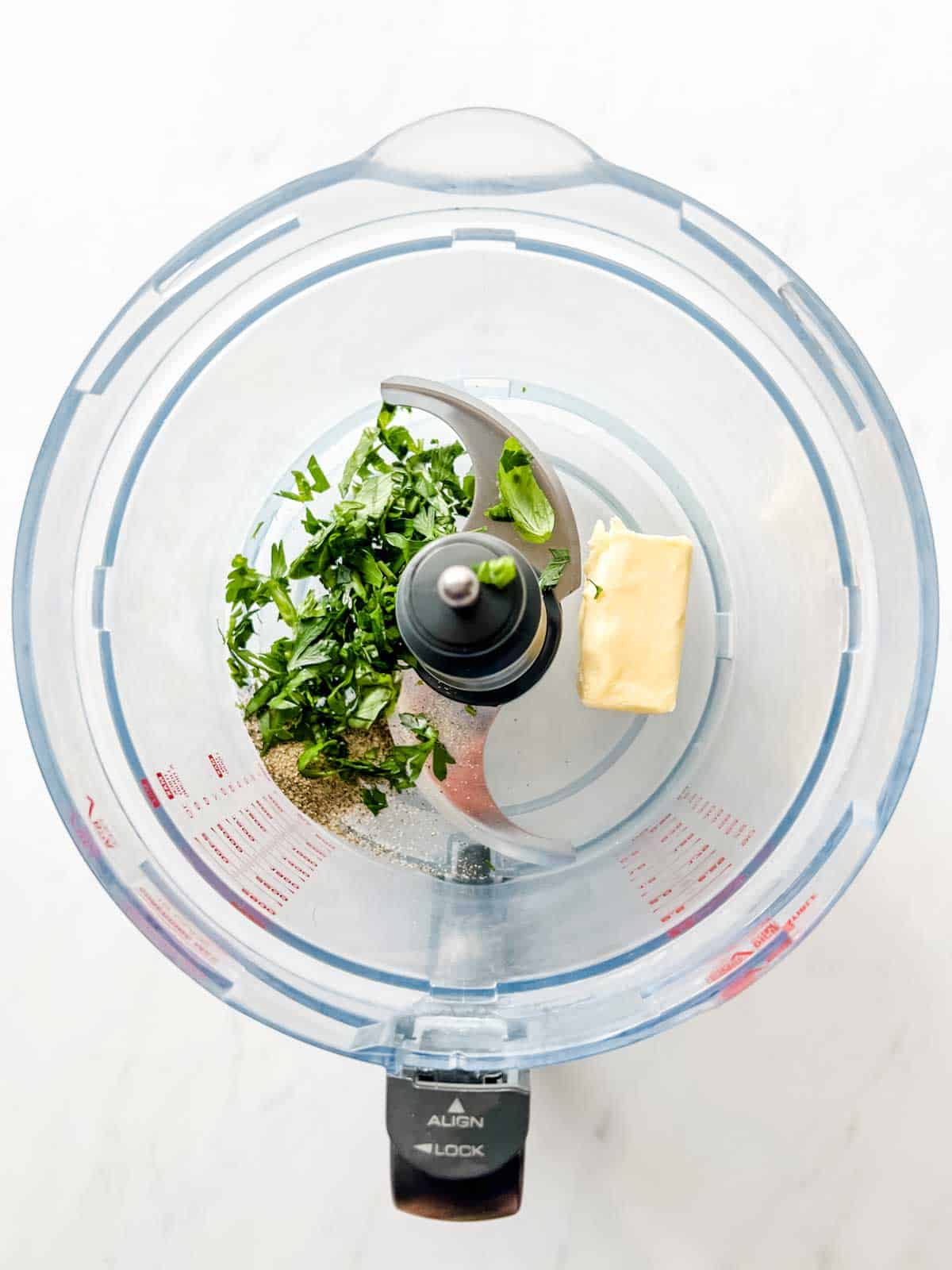 Photo of a food processor with butter, seasonings and fresh herbs.